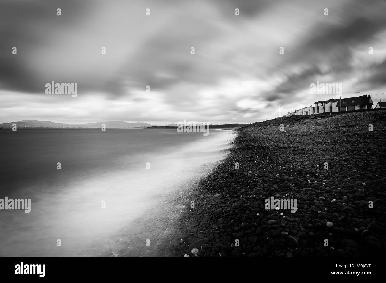 Un fantastico nord atlantico sul paesaggio un moody giorno irlandese. La città case si affacciano sulla spiaggia rocciosa e dell'oceano. Acquisite utilizzando una lunga esposizione. Foto Stock