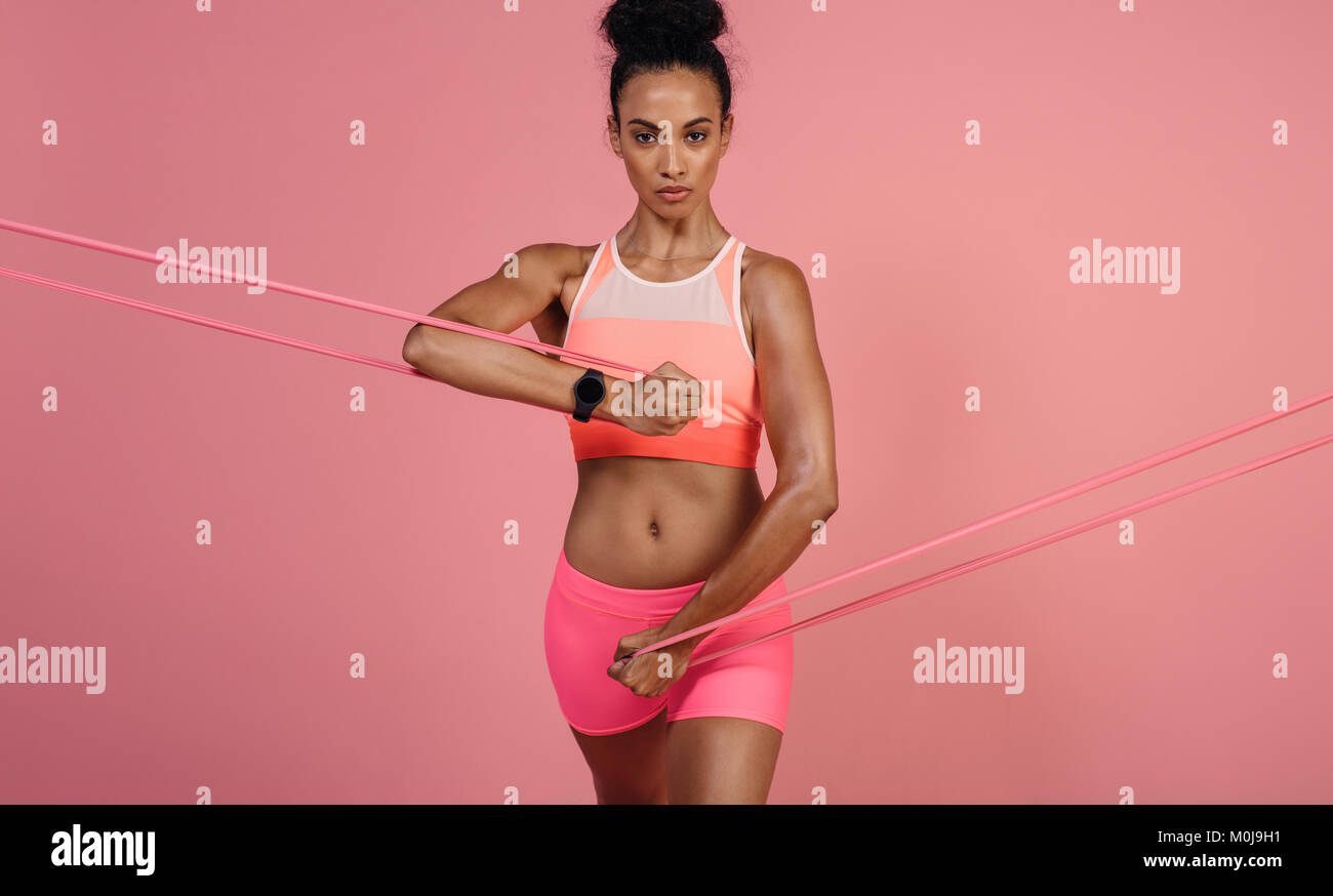 Donna difficili utilizzando una banda di resistenza nel suo esercizio di routine. Atleta femminile esercitando con banda di resistenza contro lo sfondo di colore rosa. Foto Stock