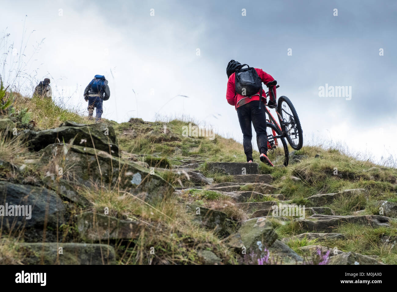 Gli escursionisti a piedi e il ciclista il trasporto di una bicicletta su una ripida collina. La scala di Giacobbe, Derbyshire, Parco Nazionale di Peak District, England, Regno Unito Foto Stock