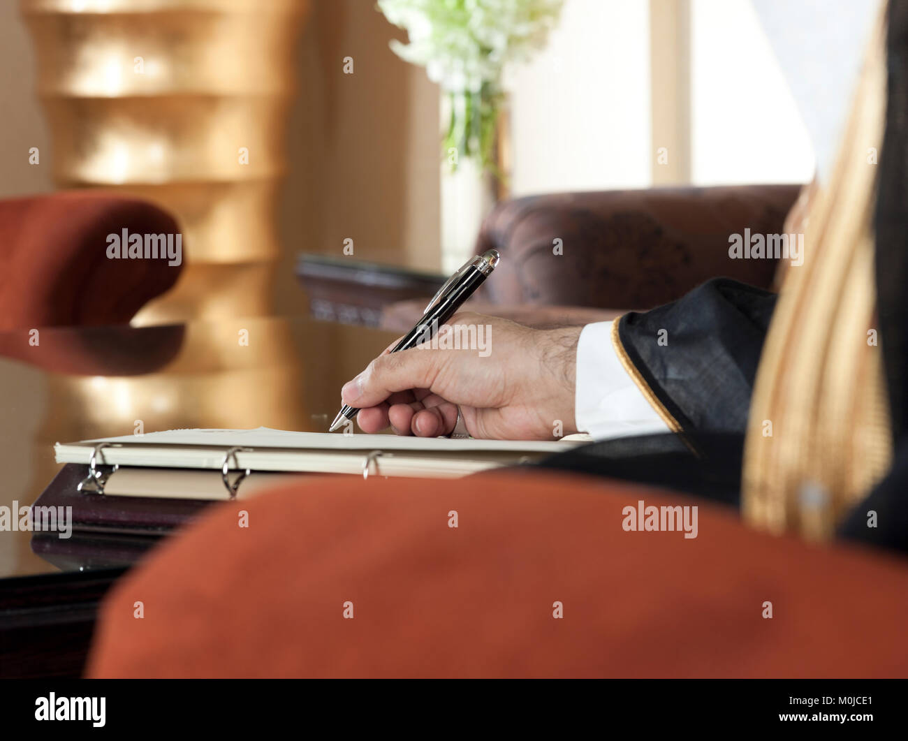 Saudi Arabian man mano che scrive su un notebook in un lussuoso ambiente domestico, indossando Arabia Thob, Ghutra e Bisht nero Foto Stock