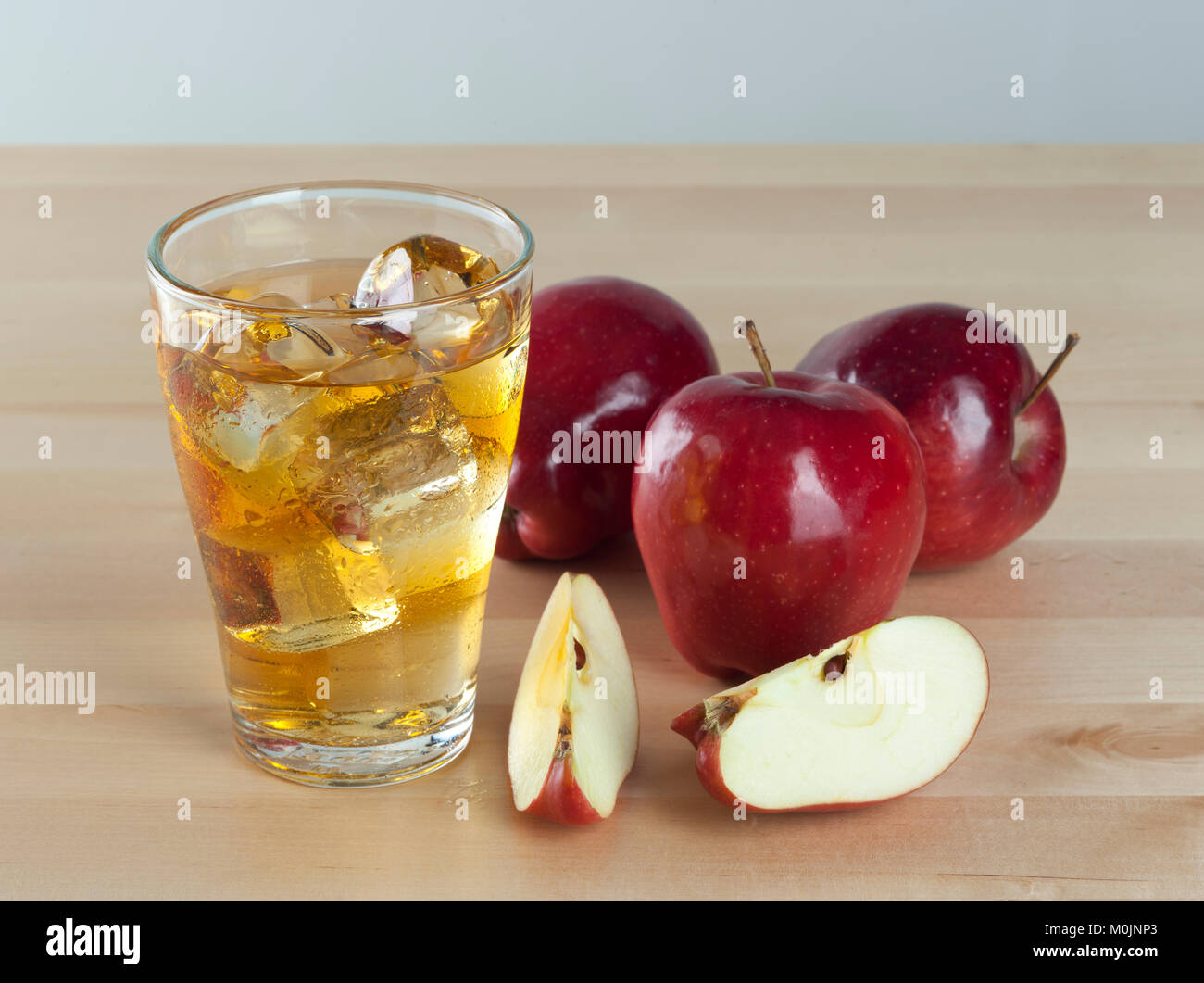 Un bicchiere di freddo fresco succo di mela con ghiaccio accanto le mele su un tavolo di legno sfondo Foto Stock