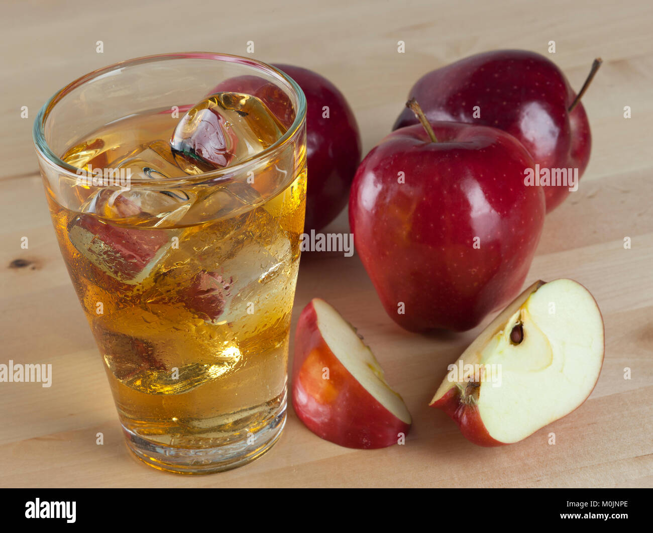 Un bicchiere di freddo fresco succo di mela con ghiaccio accanto le mele su un tavolo di legno sfondo Foto Stock
