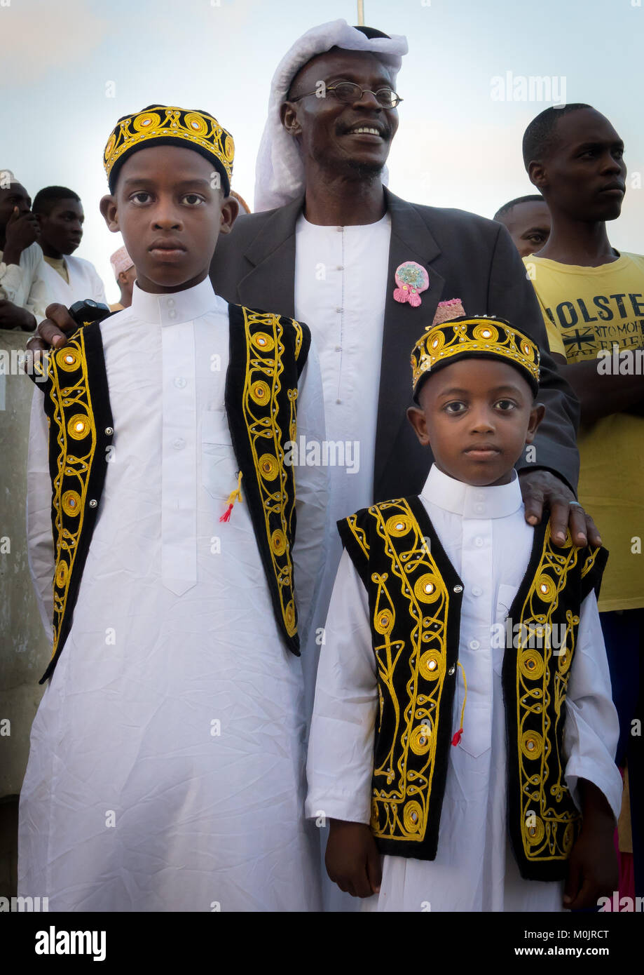 I bambini che indossano vestiti tradizionali & kufi per il mawlid festival, celebrando con il loro padre nella affollata corniche di isola di Lamu, Kenya Foto Stock