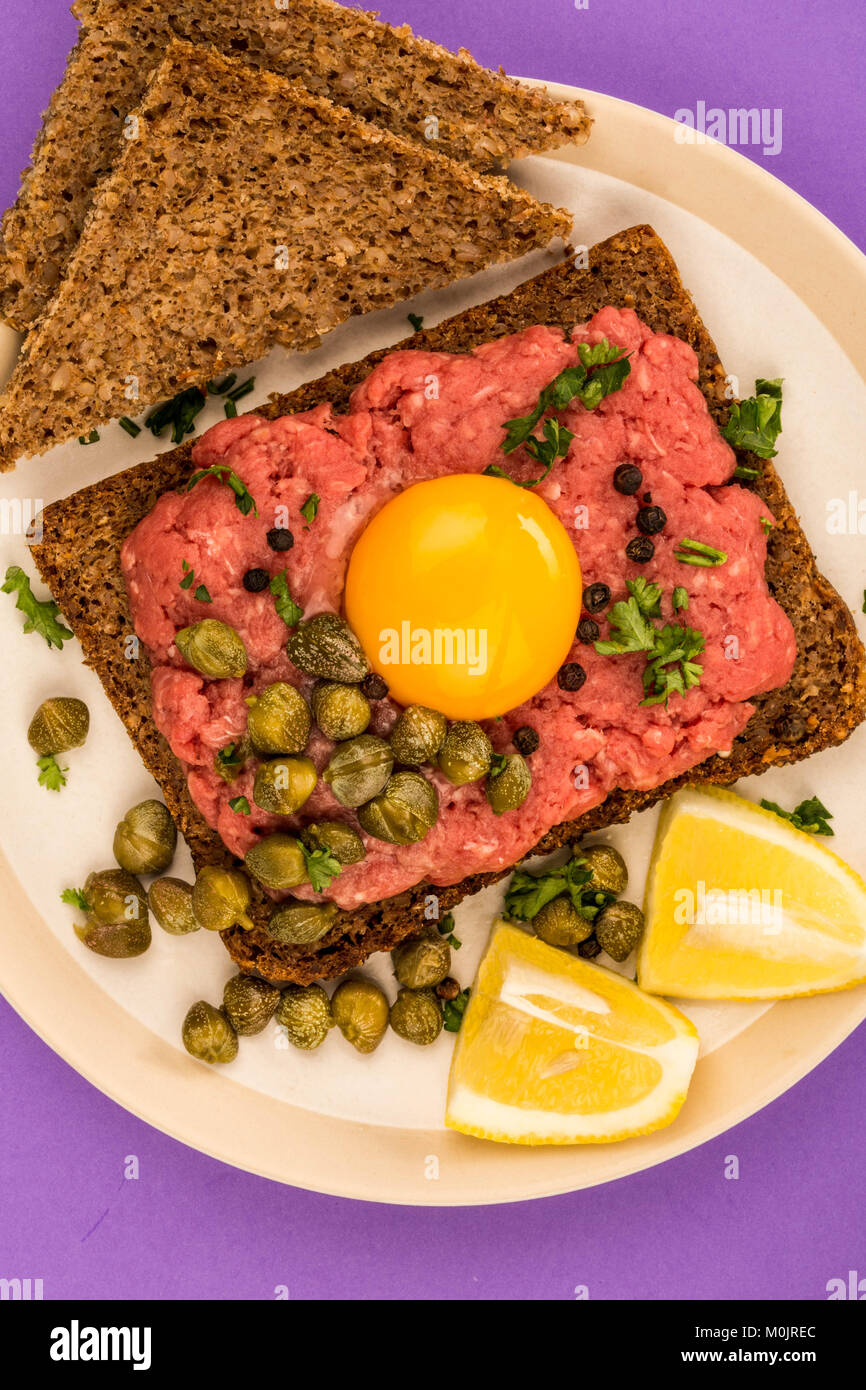 Tartare di manzo con capperi e un uovo crudo faccia aperta panino contro uno sfondo viola Foto Stock