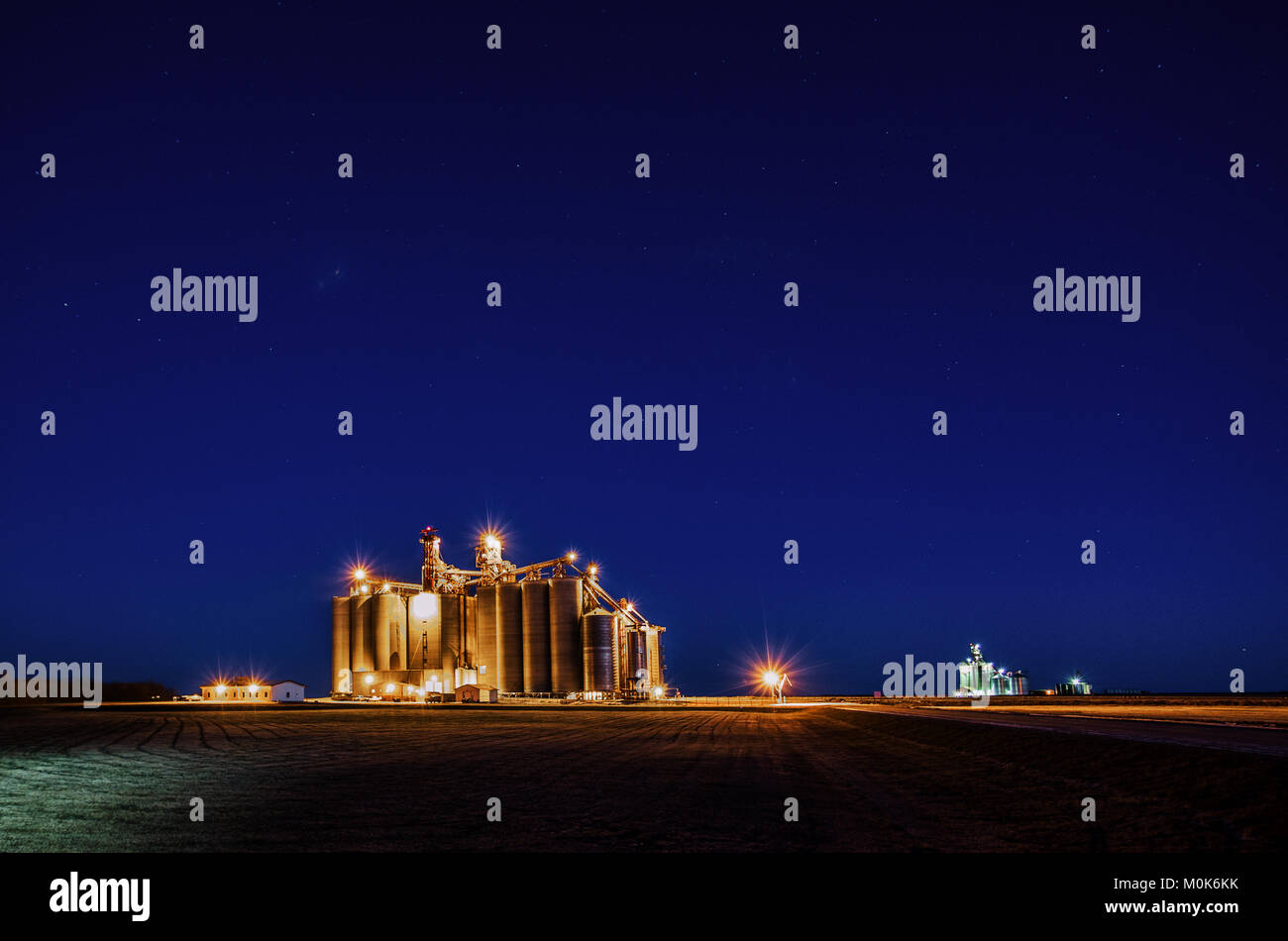 Cemento illuminato stoccaggio granella ascensori con coclee sovraccarico in un paesaggio paesaggio agricolo di notte Foto Stock