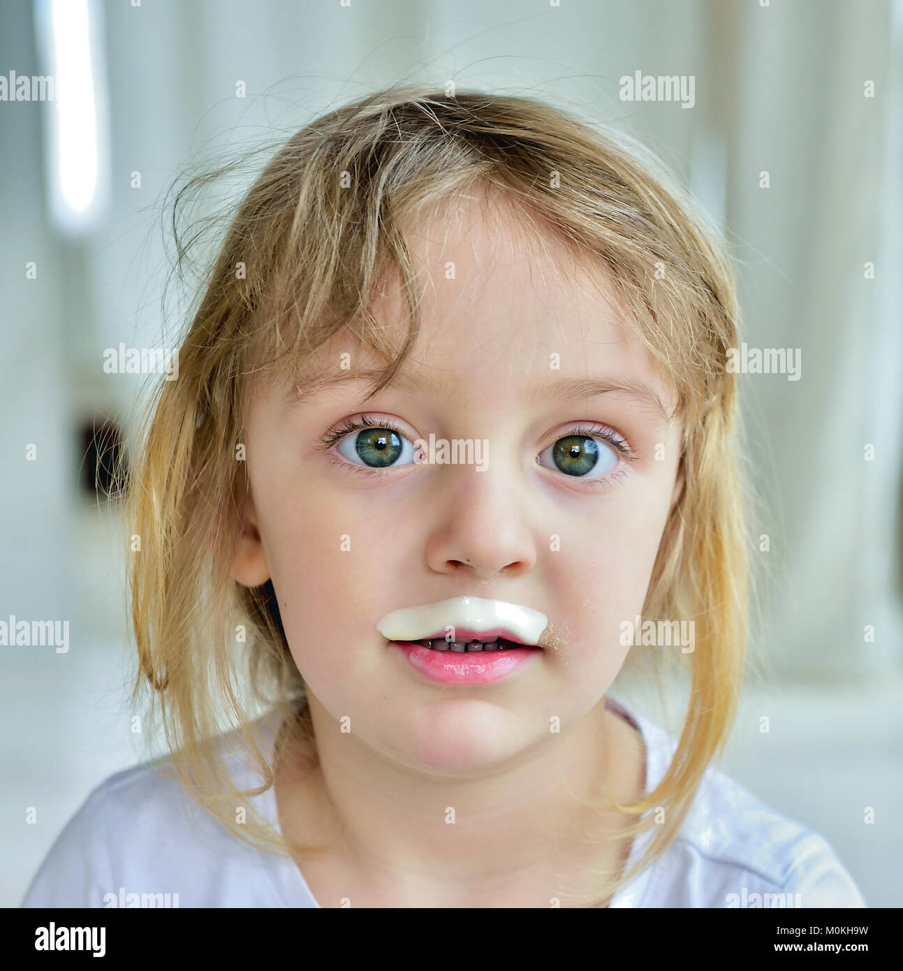 Close up divertente ritratto di carino bambina con latte baffi. Ritratto di un po' di felice ragazza con yogurt sulla faccia. Foto Stock