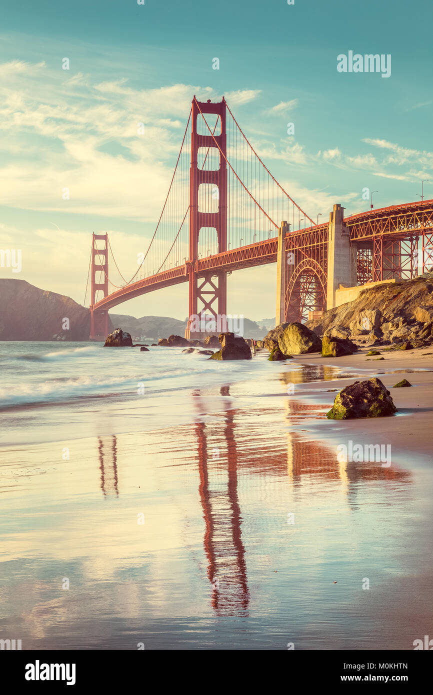 Classic vista verticale del famoso Golden Gate Bridge visto da scenic Baker Beach in beautiful Golden luce della sera in una giornata di sole con cielo blu Foto Stock