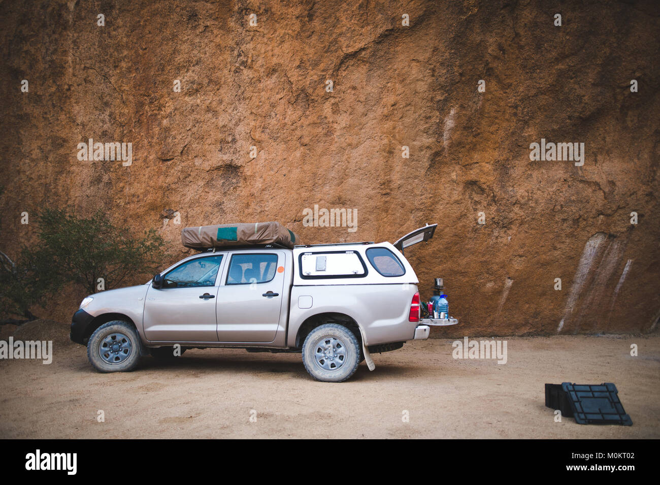 Un veicolo fuoristrada con attrezzature per il campeggio è parcheggiato a fianco di grandi formazioni rocciose nel Deserto Namibiano Foto Stock