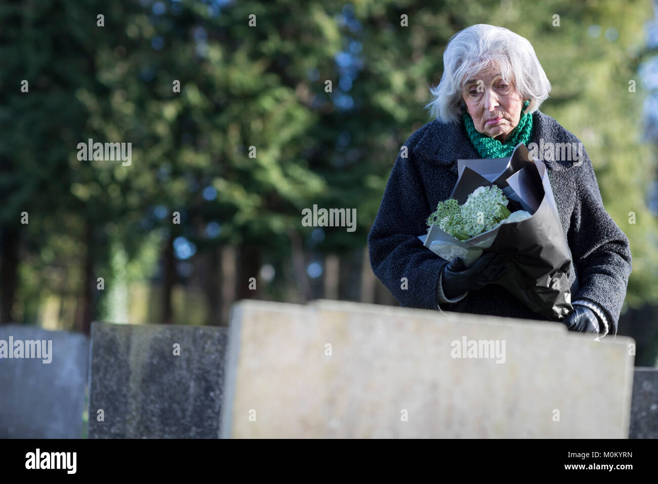 Triste Senior Donna con fiori in piedi da gravi Foto Stock