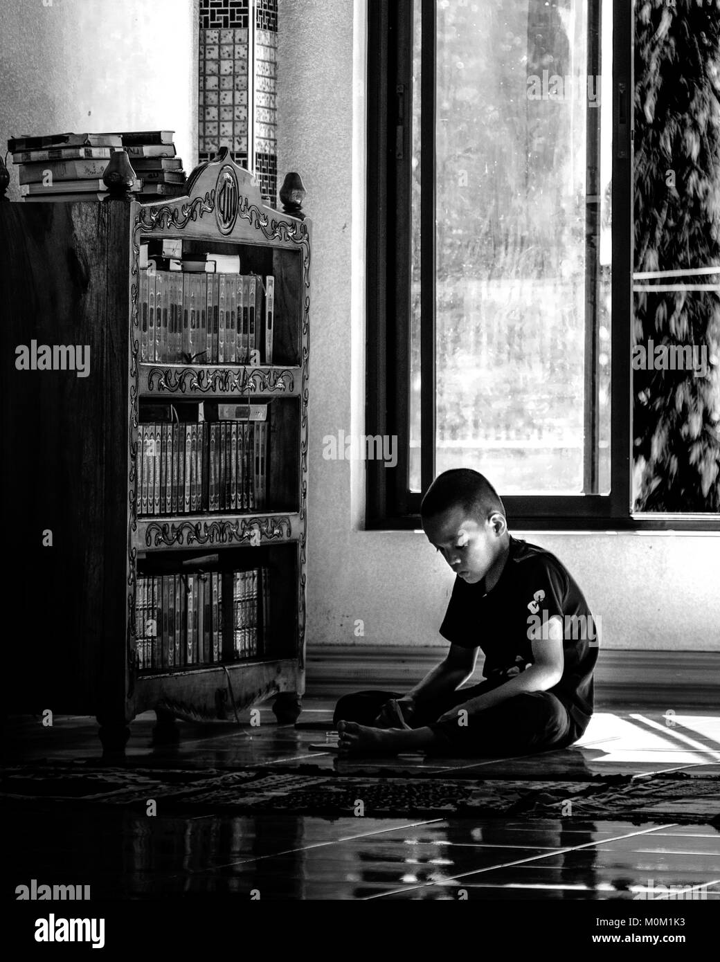 Un giovane musulmano leggendo un libro all'interno di Masjid Dimaukom noto anche come la Moschea di rosa a Maguindanao, Filippine. Foto Stock