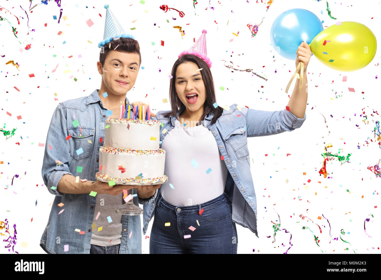 Gli adolescenti in possesso di una torta di compleanno e palloncini con i confetti streamers battenti intorno a loro isolati su sfondo bianco Foto Stock