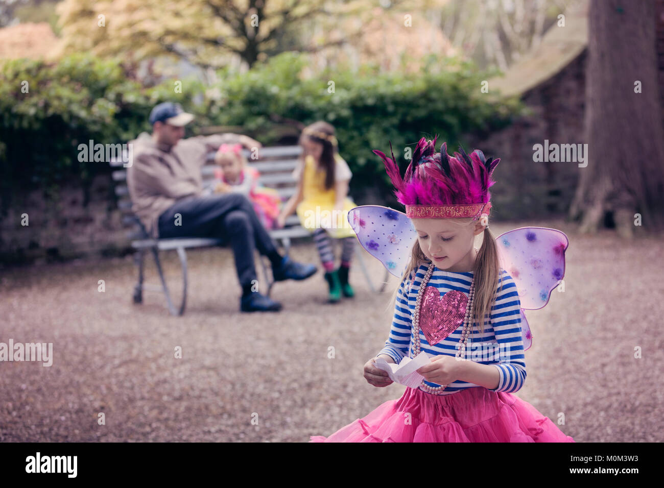Ragazza in costume fata, la lettura di una lettera con la famiglia in background Foto Stock