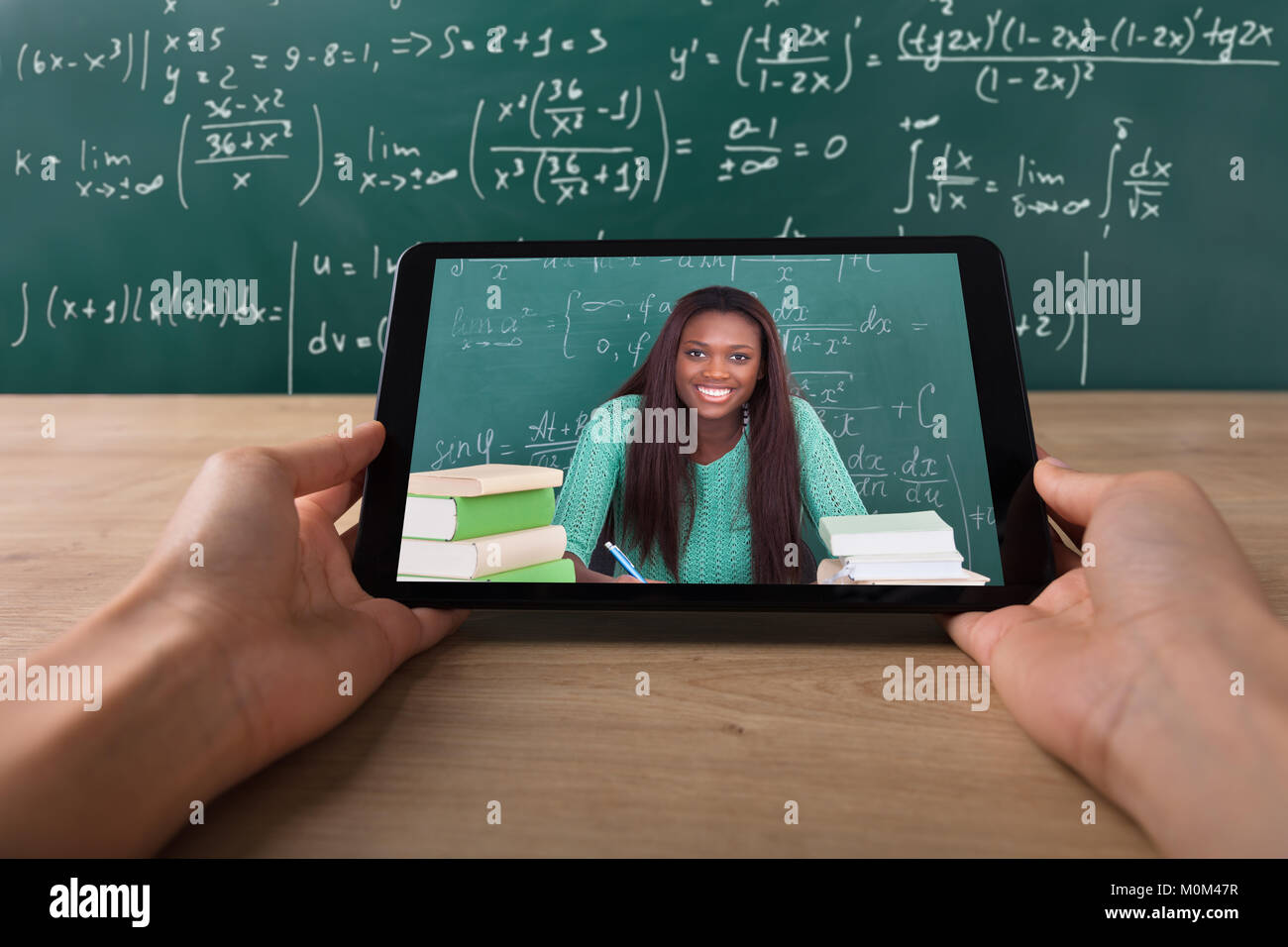 Close-up di uno studente la mano le videoconferenze con felice insegnante femmina su Tablet sulla scrivania Foto Stock