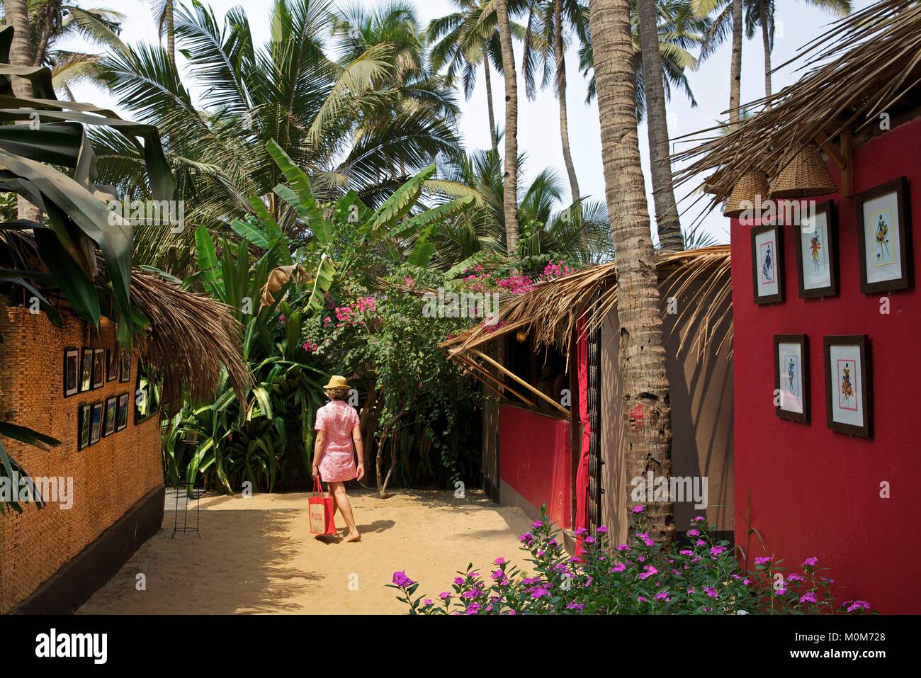L'India,Goa,Morjim beach,Donna che cammina in un vicolo di sabbia e sotto gli alberi di noce di cocco del ristorante in spiaggia la Plage Foto Stock