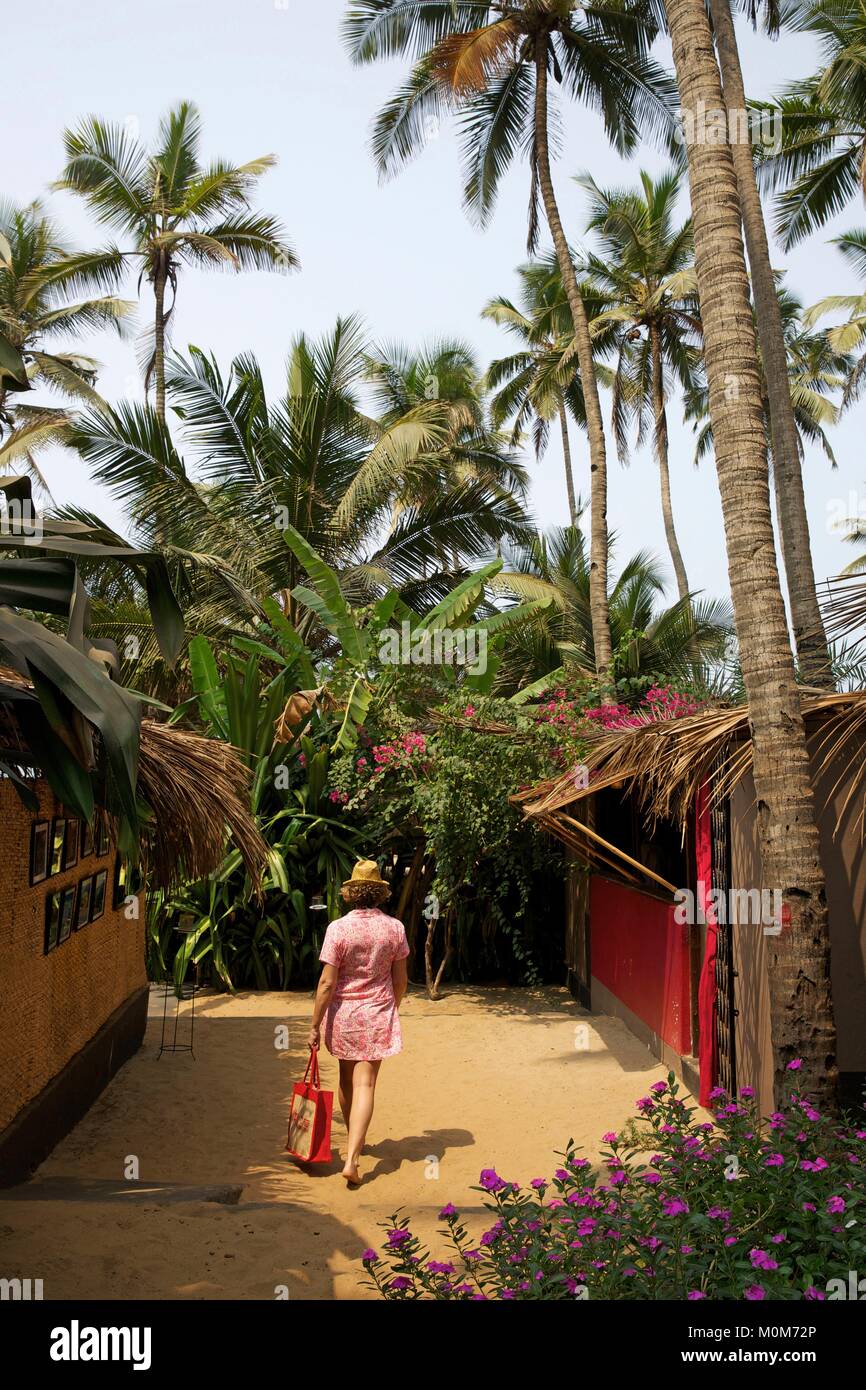 L'India,Goa,Morjim beach,Donna che cammina in un vicolo di sabbia e sotto gli alberi di noce di cocco del ristorante in spiaggia la Plage Foto Stock