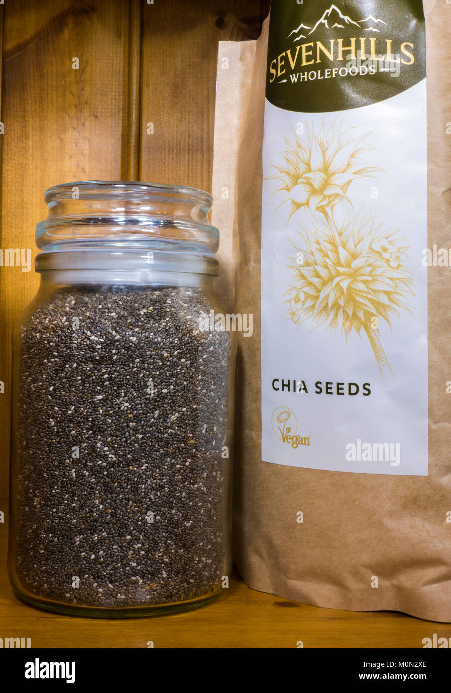 Chia (semi di salvia hispanica). Organico, non cotte, alto in proteina, vegan, super. In un pacchetto e contenitore in vetro su un ripiano in un armadio di pino. Foto Stock