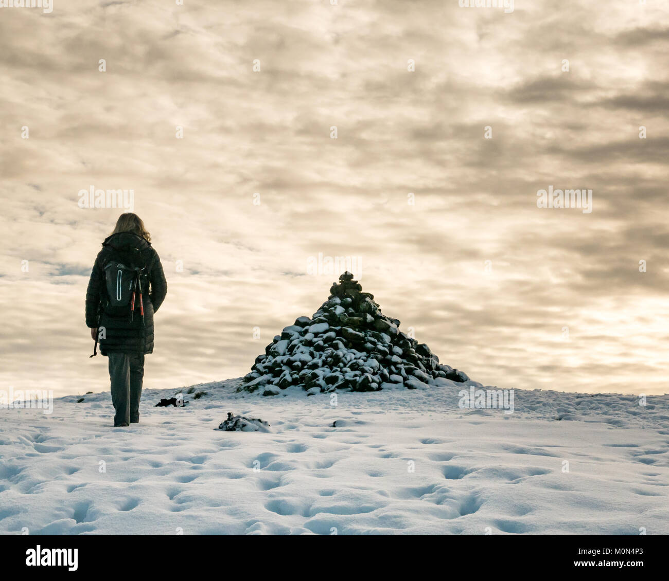La donna a piedi nella neve in salita su sentiero tra Langbank e Kilmacolm verso la coperta di neve cairn, Strathclyde, Scozia, con chiazze cielo nuvoloso Foto Stock