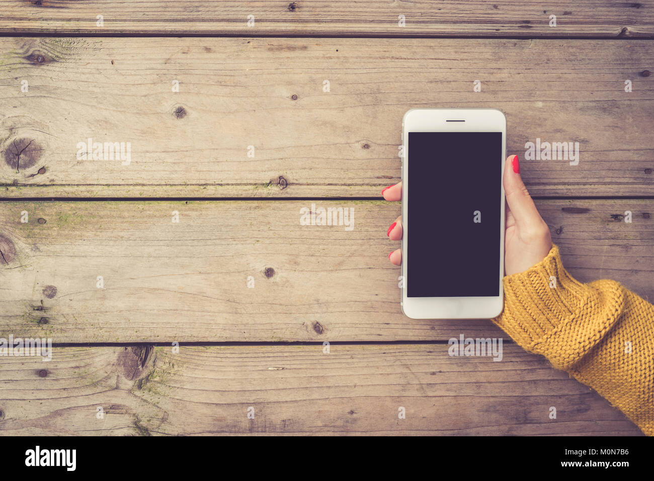 Donna che utilizza un smartphone bianco in un maglione pesante Foto Stock