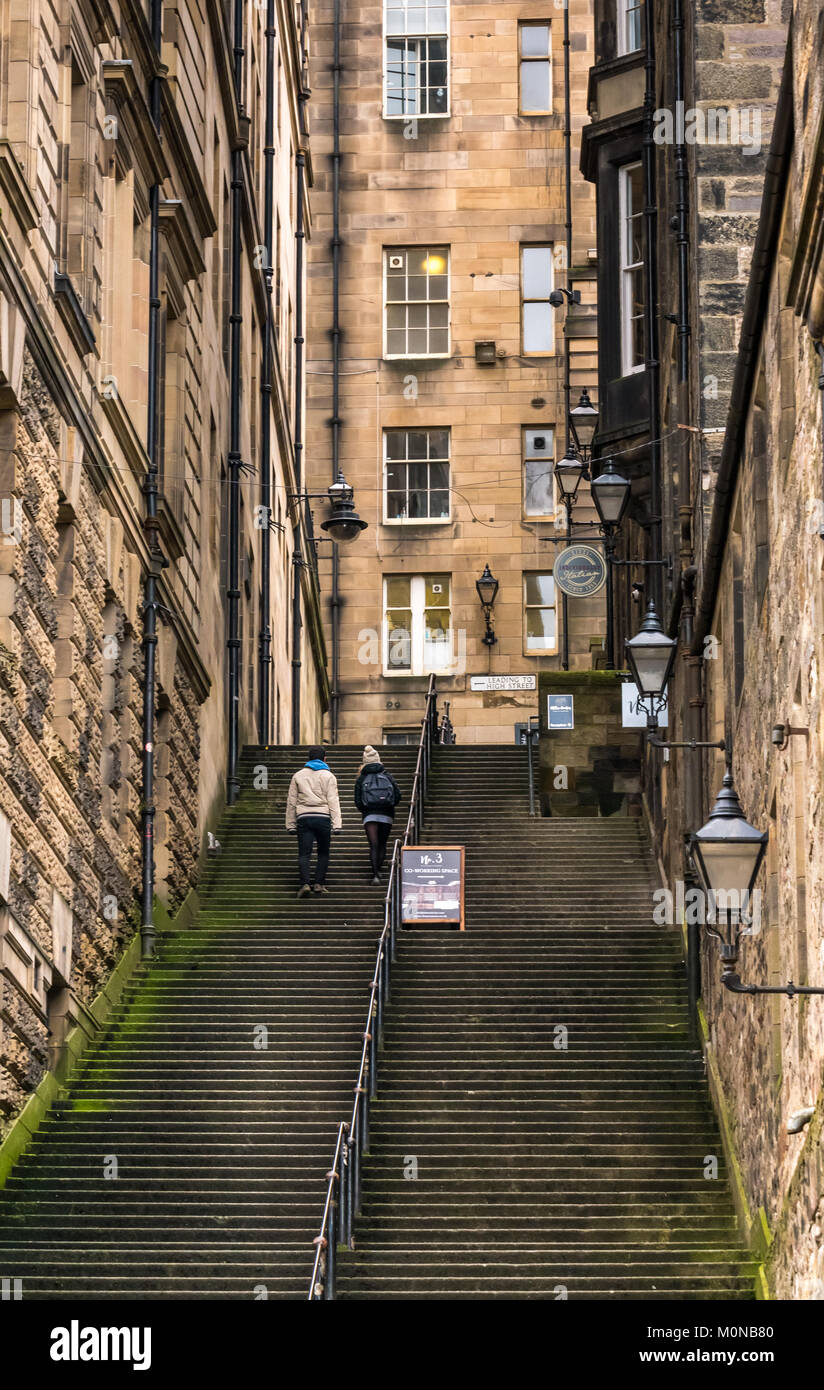 Giovane arrampicate ripide scale Warriston vicino, Cockburn Street a Royal Mile di Edimburgo, Scozia con tenement edifici e in vecchio stile lampade Foto Stock