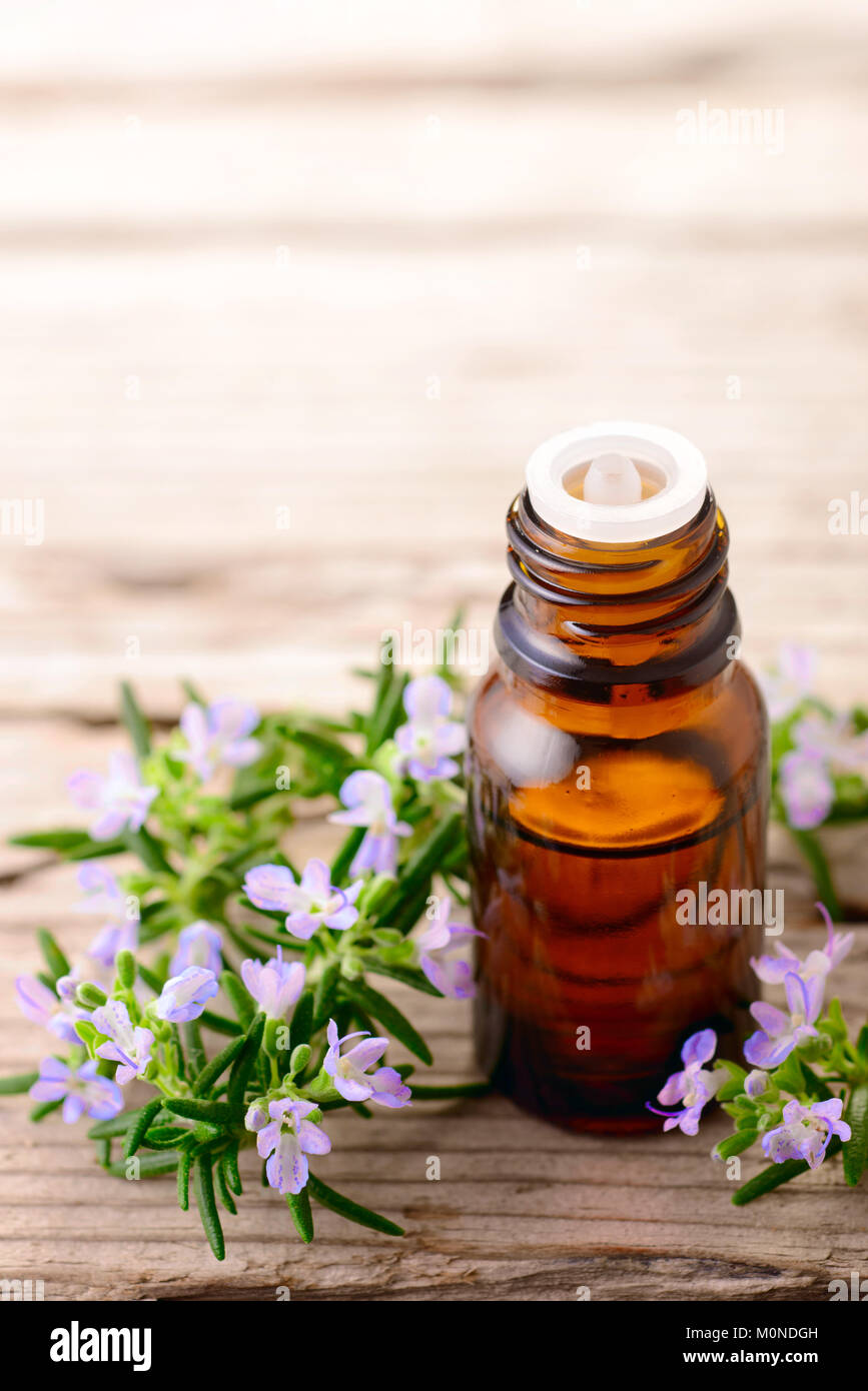 Olio essenziale di rosmarino e fiori sulla tavola di legno Foto Stock