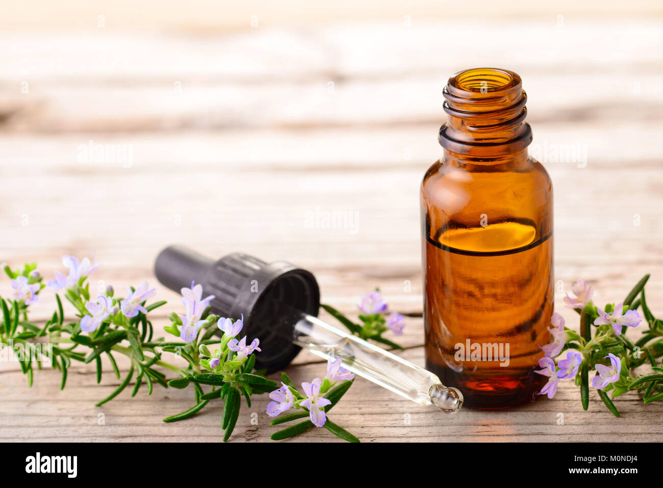 Olio essenziale di rosmarino e fiori sulla tavola di legno Foto Stock