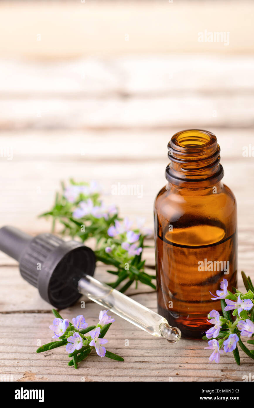 Olio essenziale di rosmarino e fiori sulla tavola di legno Foto Stock