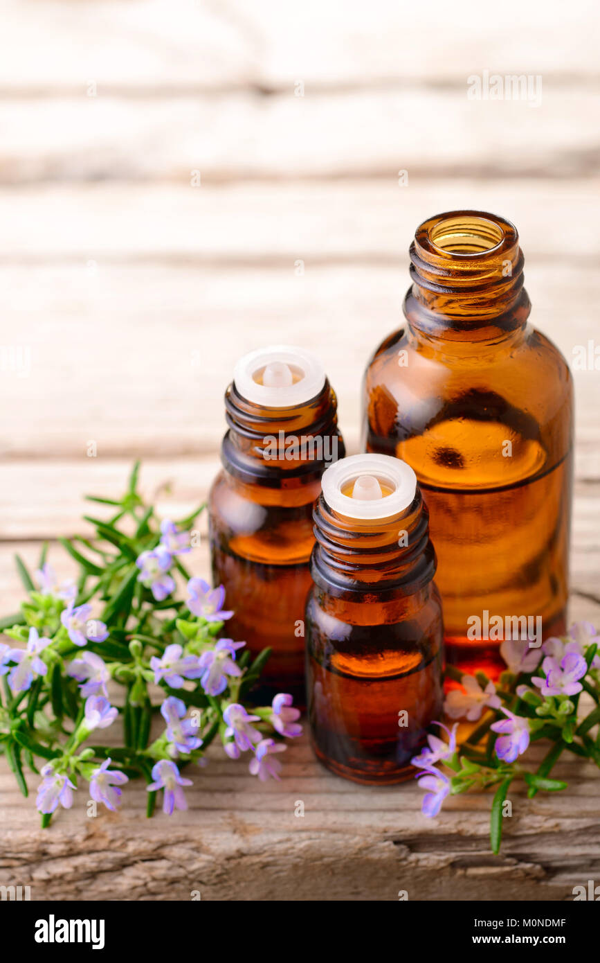 Olio essenziale di rosmarino e fiori sulla tavola di legno Foto Stock