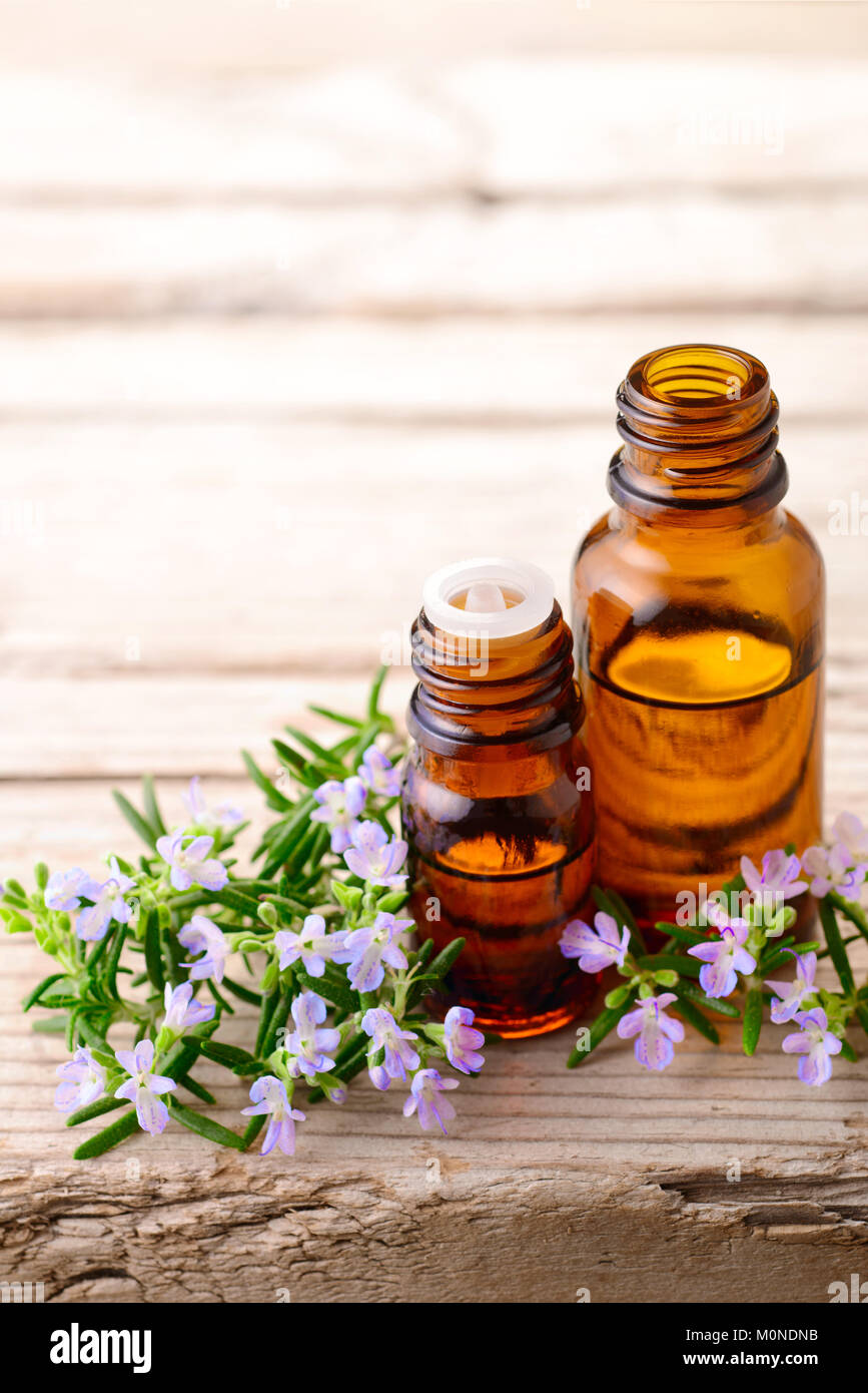 Olio essenziale di rosmarino e fiori sulla tavola di legno Foto Stock
