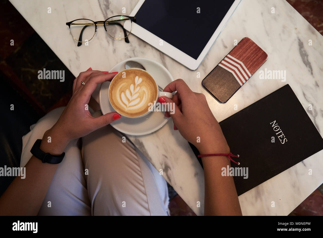 Da sopra vista di una tazza di caffè sostenuto da mani femminili e circondato dalla tecnologia in una tavola di marmo. Foto Stock