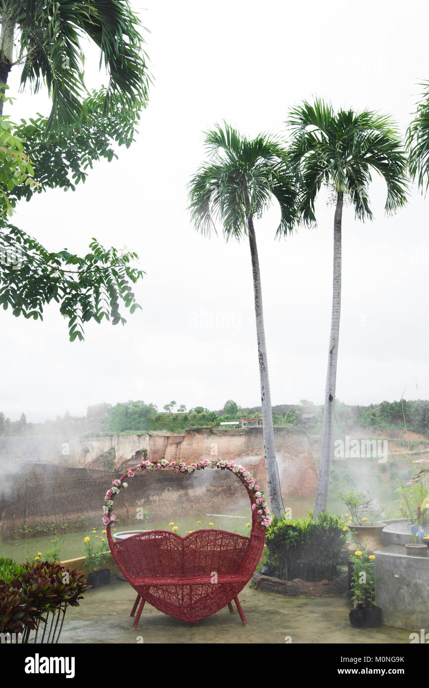 Panca con una forma a suola in rosso decorato con fiori contro un paesaggio tropicale con palme in Thailandia. Foto Stock