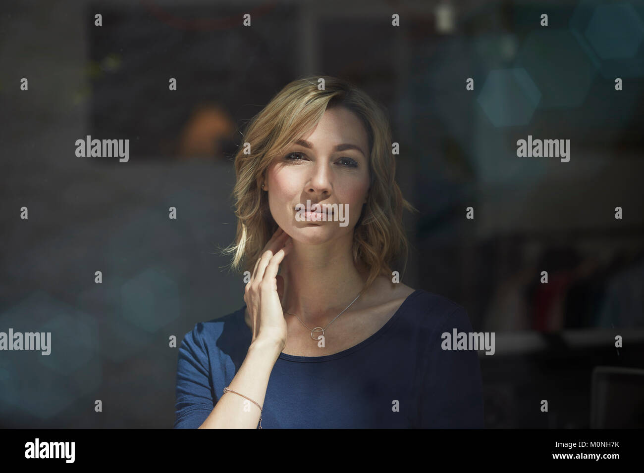 Ritratto di donna bionda dietro vetro, mano sul collo Foto Stock