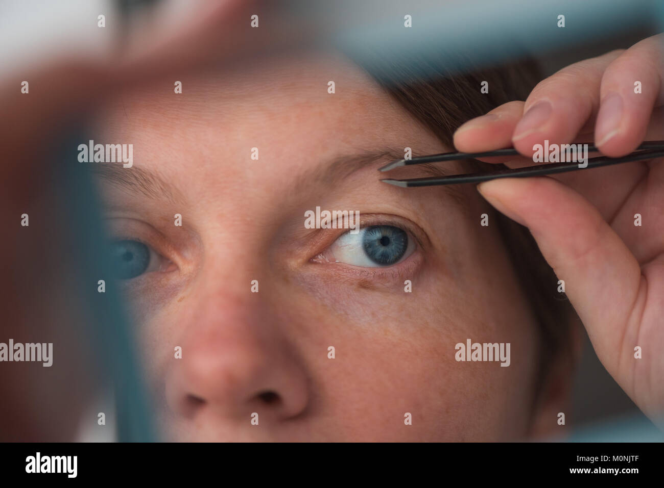 Donna spiumatura sopracciglia con pinzette dalla finestra, il fuoco selettivo Foto Stock