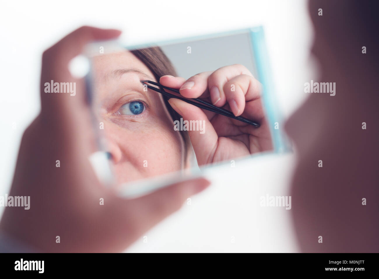 Donna spiumatura sopracciglia con pinzette dalla finestra, il fuoco selettivo Foto Stock