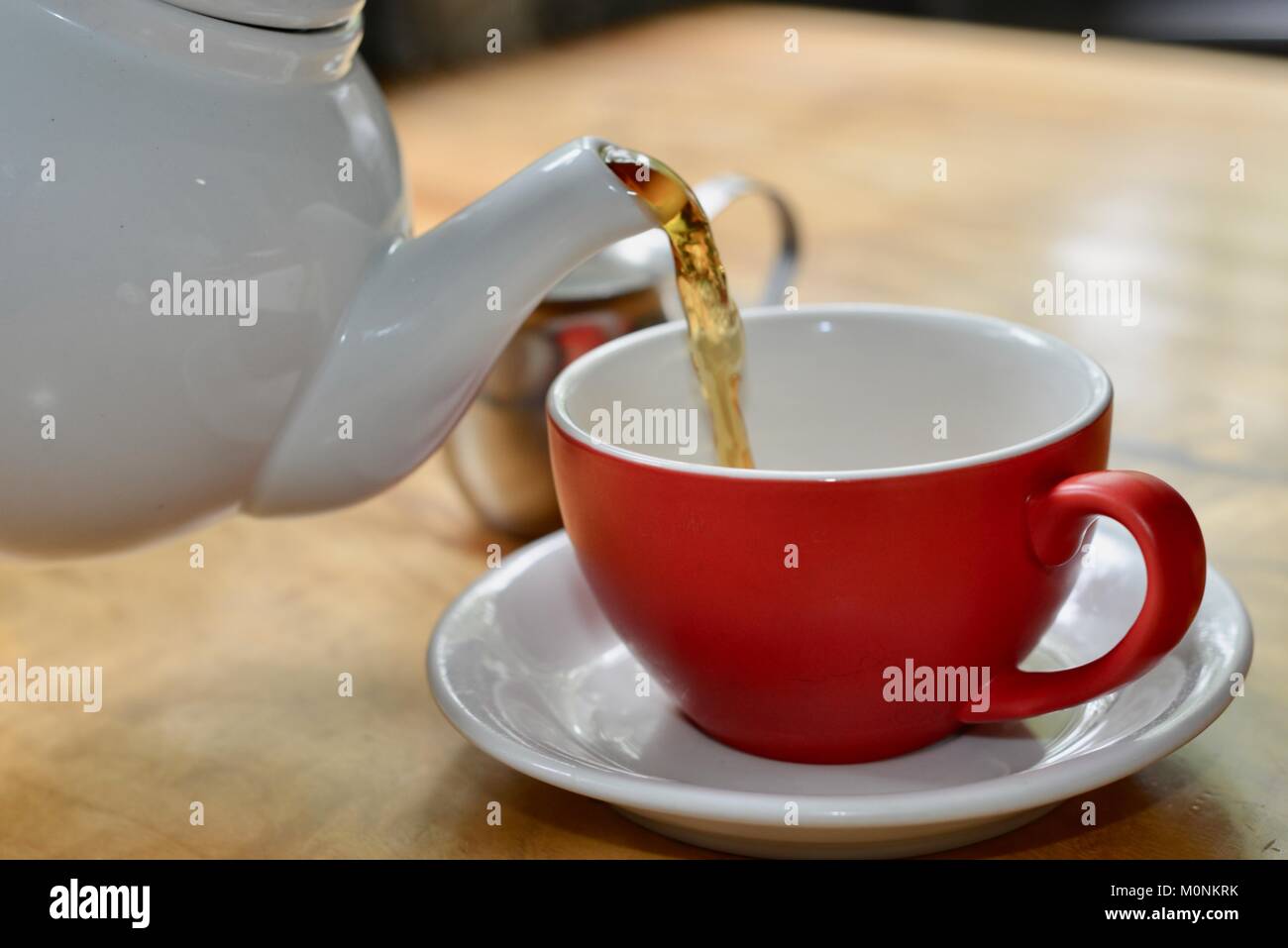 Il tè nero che viene colato bianco teiera ceramica in un rosso tazza con piattino bianco, Herveys patrimonio di gamma camere di tè, Queensland, Australia Foto Stock