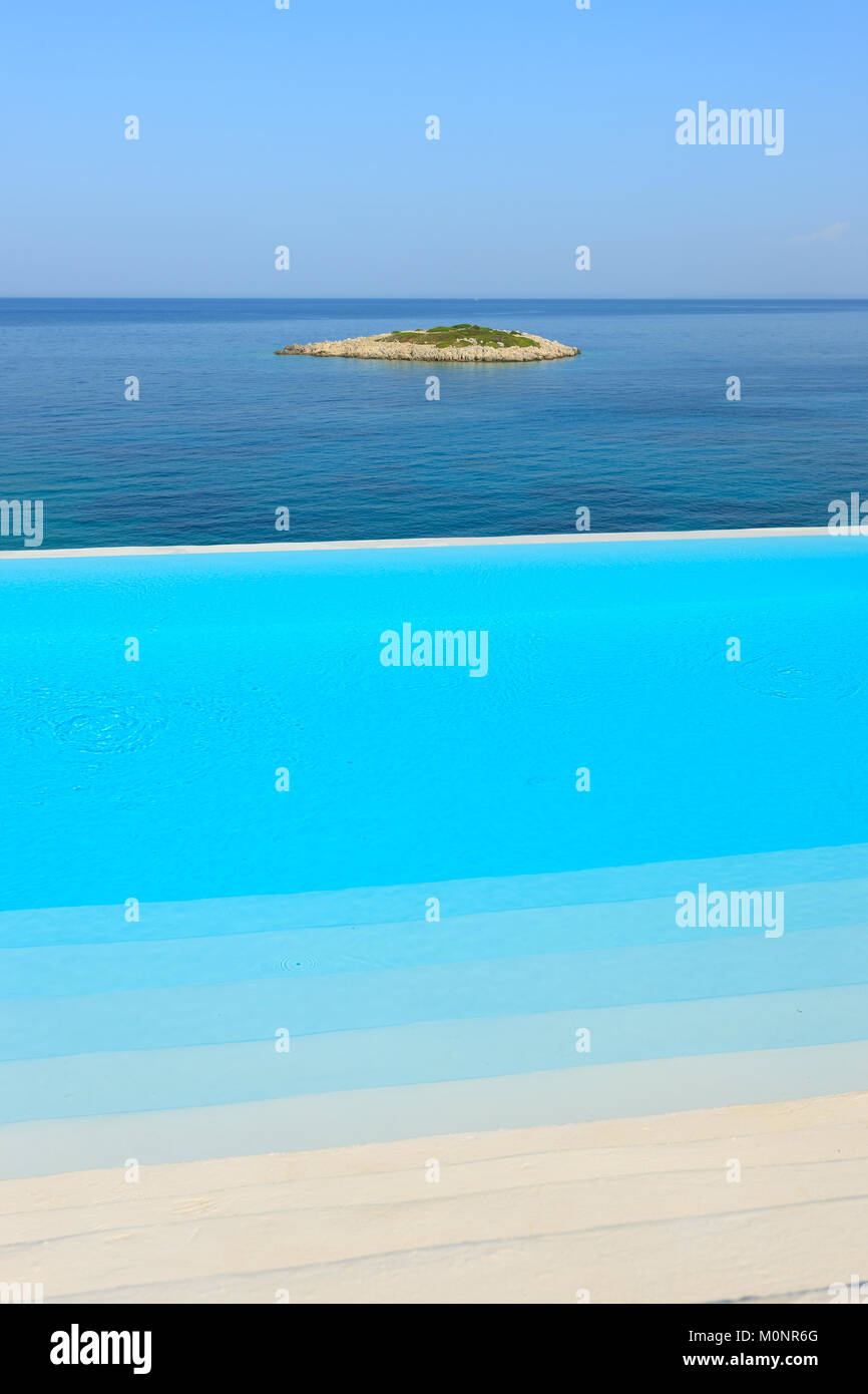 Parte di una piscina e di una piccola isola in background è vista in un resort estivo in Grecia Foto Stock