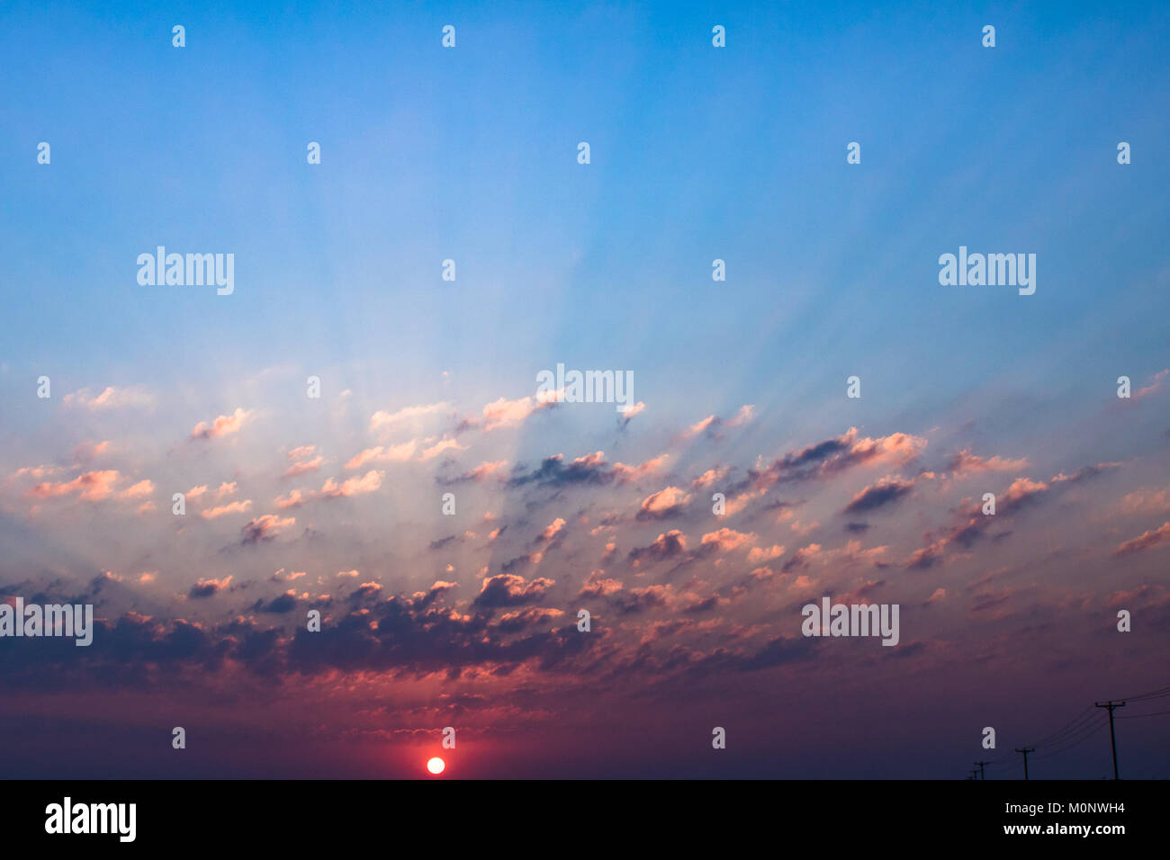 La luce del tramonto penetra attraverso le nuvole causando innumerevoli raggi di luce. Foto Stock