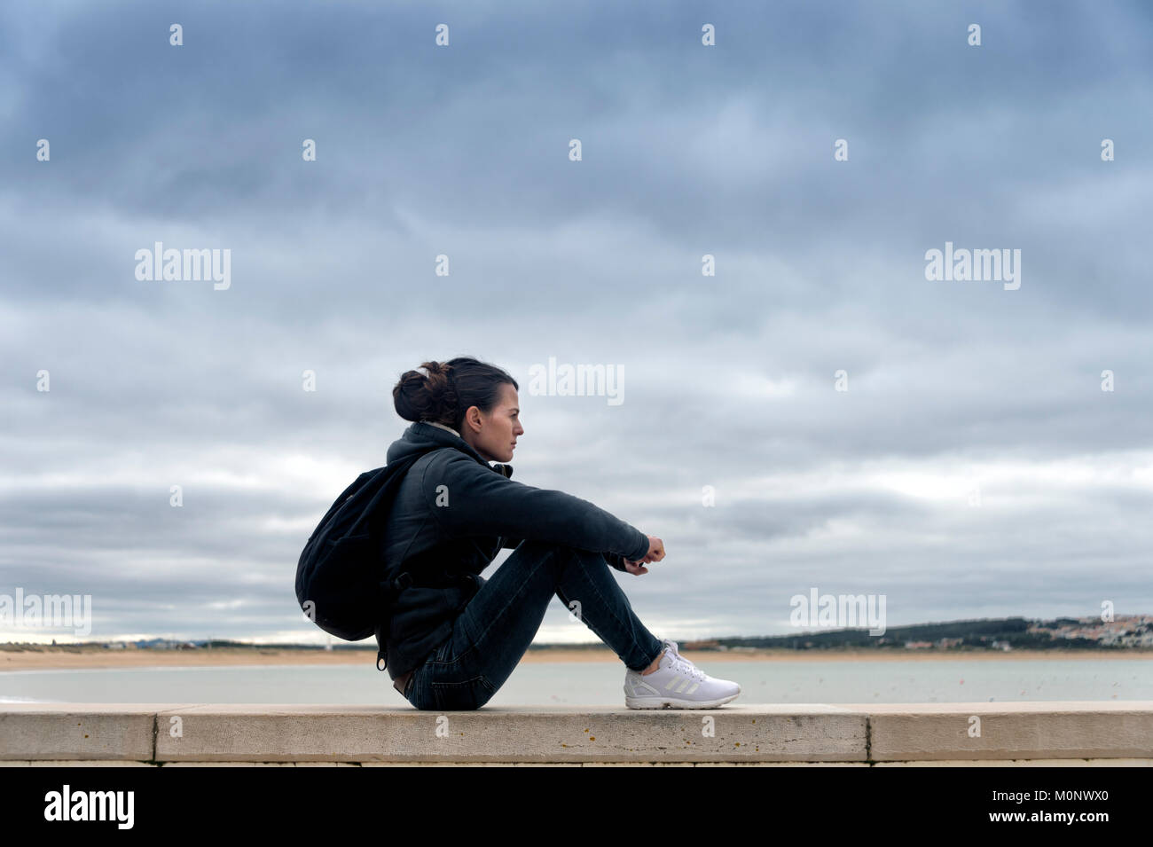 Donna seduta su un muro accanto all acqua, indossando uno zaino di riposo. Foto Stock