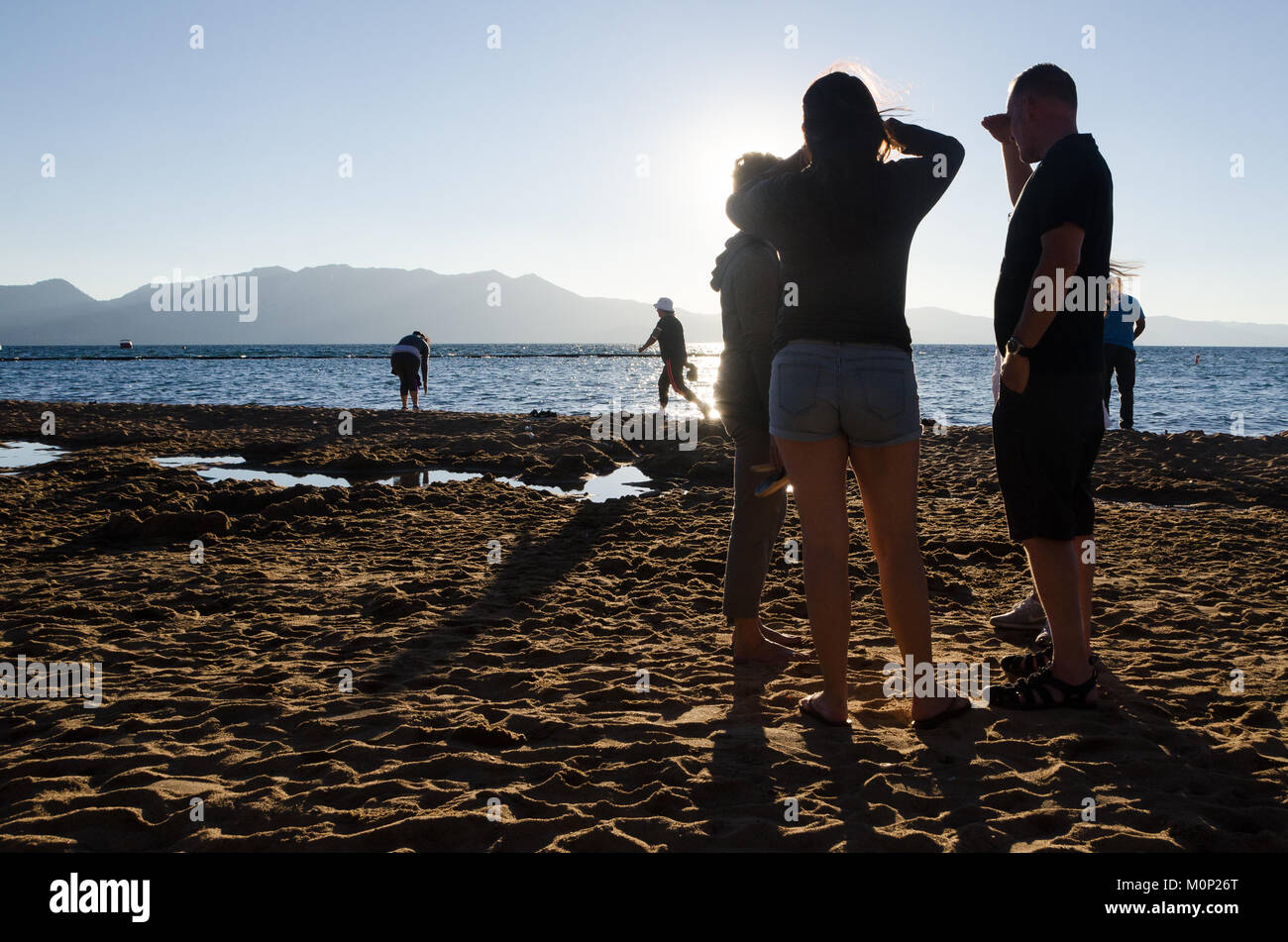 Famiglia stand parlando sul lato lago spiaggia persone giocare lungo il lungomare - Lake Tahoe, Stati Uniti Foto Stock
