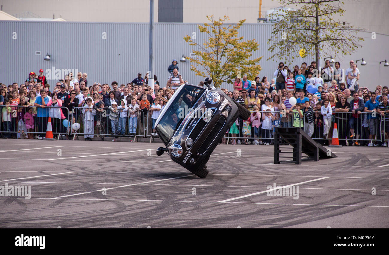 La folla guarda un stunt driver in un nuova BMW mini drive su due ruote. Foto Stock