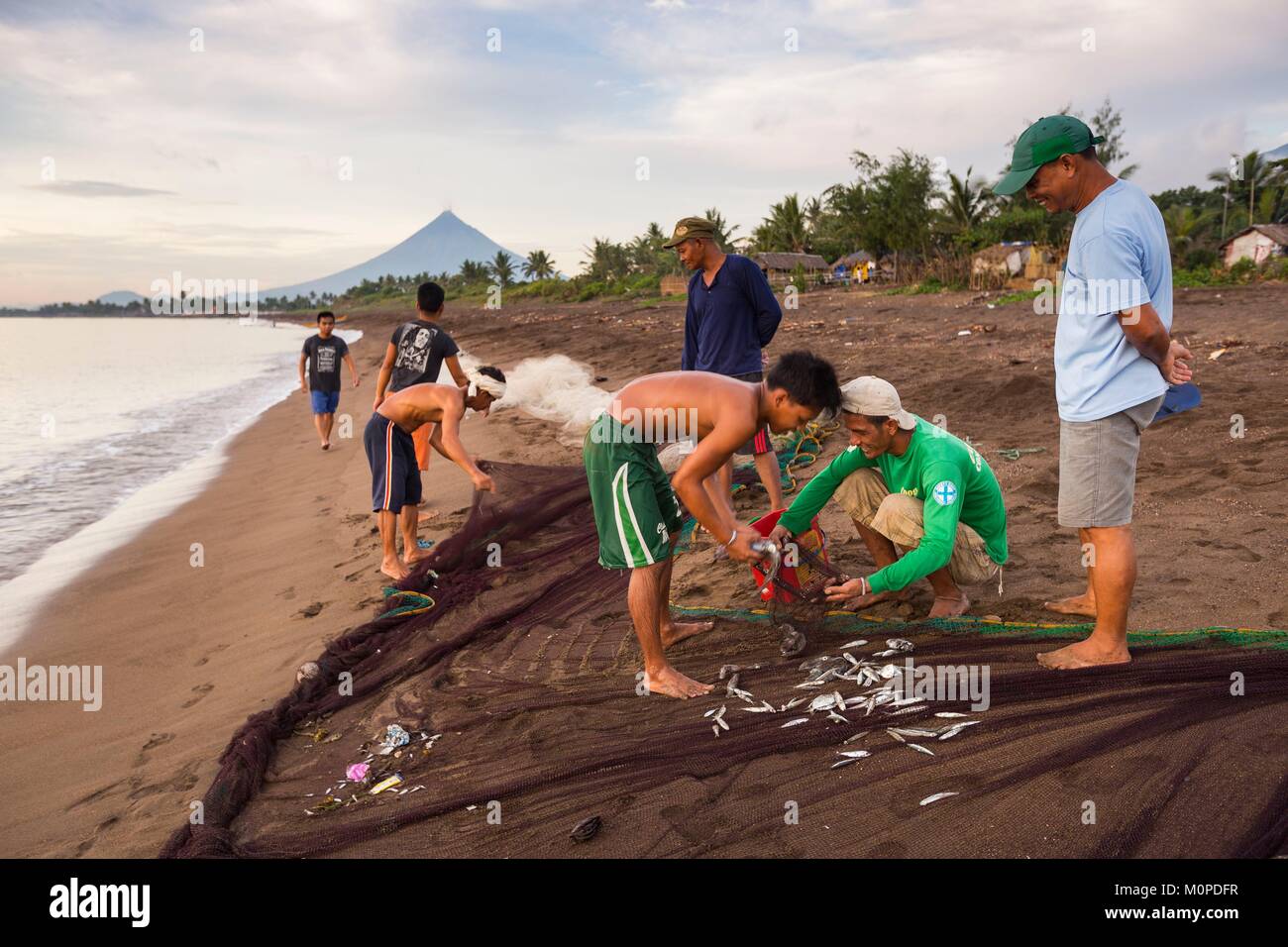 Filippine,Luzon,Albay provincia,Tiwi,pescatori portando una Tutina in rete sulla spiaggia con il vulcano Mayon nella massa posteriore Foto Stock