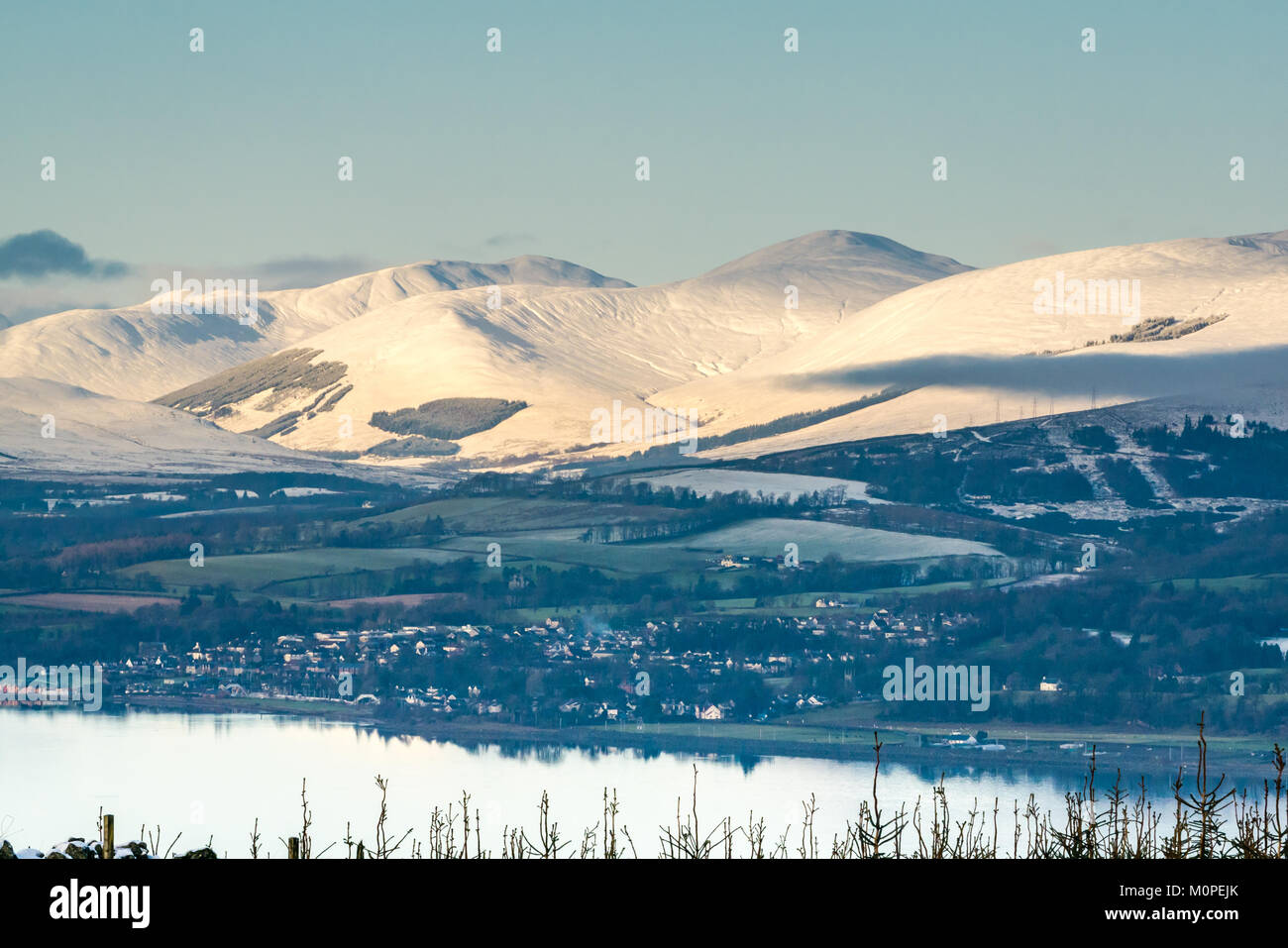 Scena invernale attraverso il fiume Clyde dalla collina sopra Langbank. Montagne coperte di neve, cielo blu e acque calme nella luce della sera, Scotland, Regno Unito Foto Stock