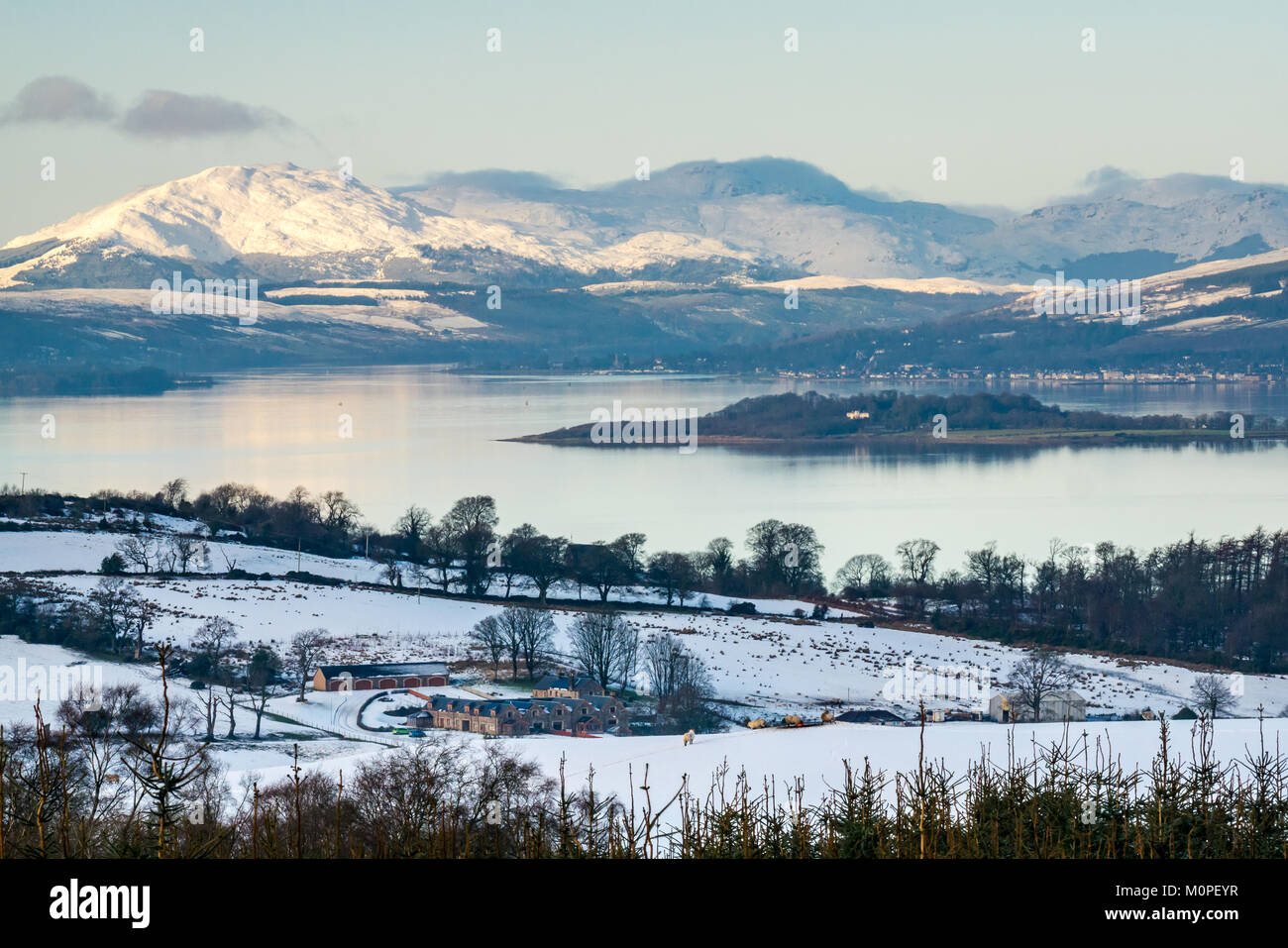 Scena invernale attraverso il fiume Clyde dalla collina sopra Langbank. Montagne coperte di neve, cielo blu e acque calme nella luce della sera, Scotland, Regno Unito Foto Stock