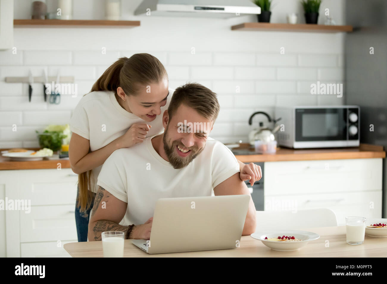 Felice coppia giovane utilizzando laptop insieme in cucina Foto Stock