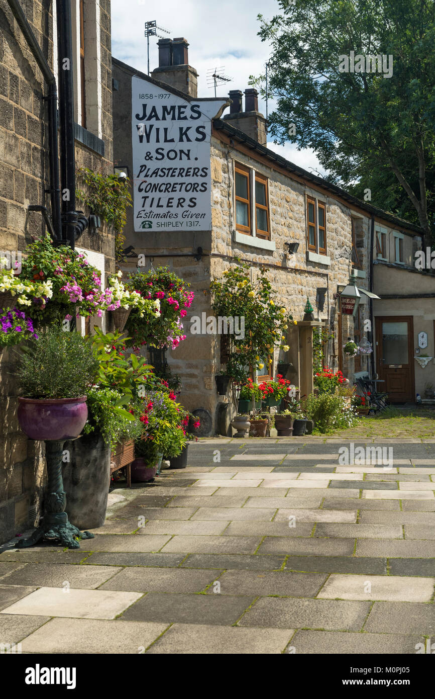 Piccolo angolo di Baildon storico con il pittoresco pietra, soleggiato cottages, fiori colorati nelle piantatrici & ghost segno sulla parete - West Yorkshire, Inghilterra, Regno Unito. Foto Stock