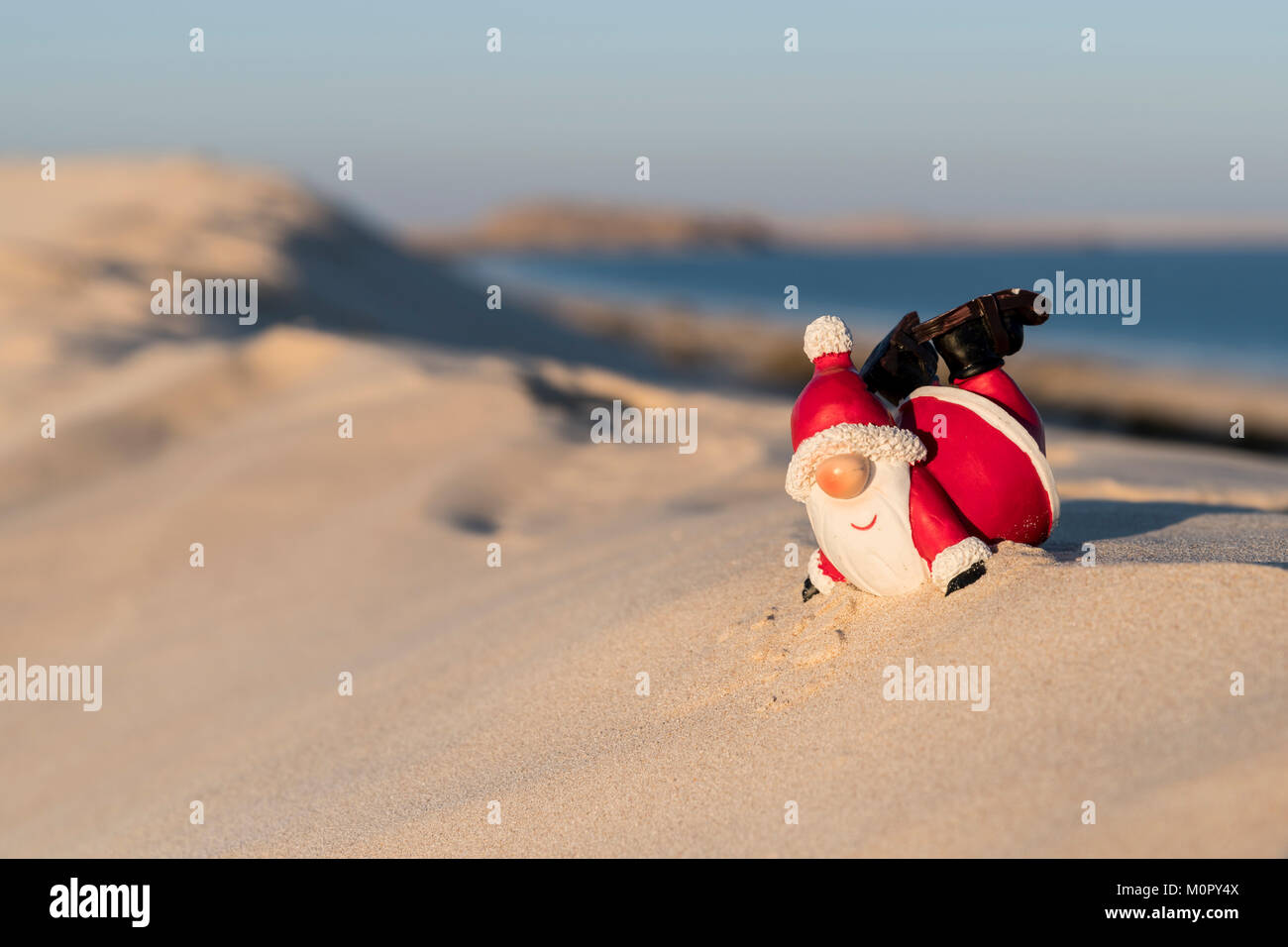 La figura di Babbo Natale esegue mosse acrobatiche su una spiaggia, con l'oceano che si estende alle spalle, mescolando allegria festosa con un divertente sfondo marino Foto Stock