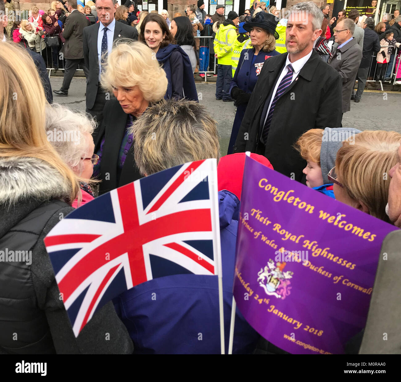 Congleton, Cheshire, Inghilterra, Regno Unito. Il 25 gennaio 2018. Camilla, duchessa di Cornovaglia saluta ben wishers in Congleton Centro Città (Cheshire Regno Unito), come la folla onda bandiere commemorative recanti un sottosopra Union Jack - un simbolo di angoscia. La coppia reale sono state visitando il Cheshire città mercato di visitare i progetti comunitari, festeggiano 700 anni avente un sindaco e svelano scultore Amy Goodman della statua commemora il Treo, un esplosivi sniffer cane, che ha servito in Afghanistan. Dopo aver attraversato la strada a visitare il Principe di Galles pub, giovane chattato e scosse le mani con i visitatori. Foto Stock