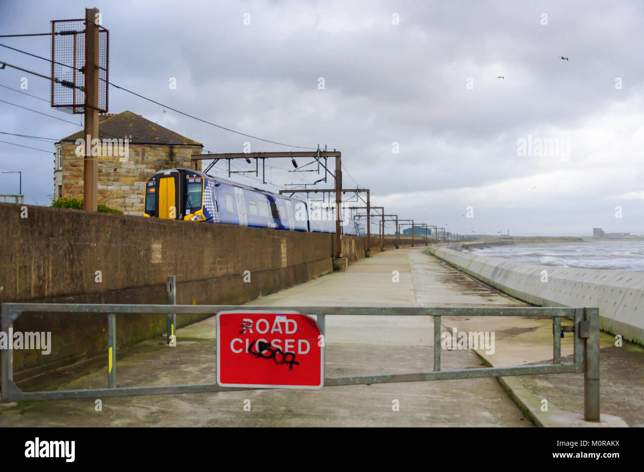 Saltcoats, Scotland, Regno Unito. Il 24 gennaio 2018. Regno Unito Meteo: un treno che passa attraverso Saltcoats viaggi prossima alla linea di costa come alta venti onde causare il crash di contro la parete del mare. La strada è chiusa per motivi di sicurezza. Tempesta Georgina è il settimo denominato storm della stagione ed è previsto per portare alta il vento e la pioggia est spazzando in tutta la Gran Bretagna. Credito: Berretto Alamy/Live News Foto Stock