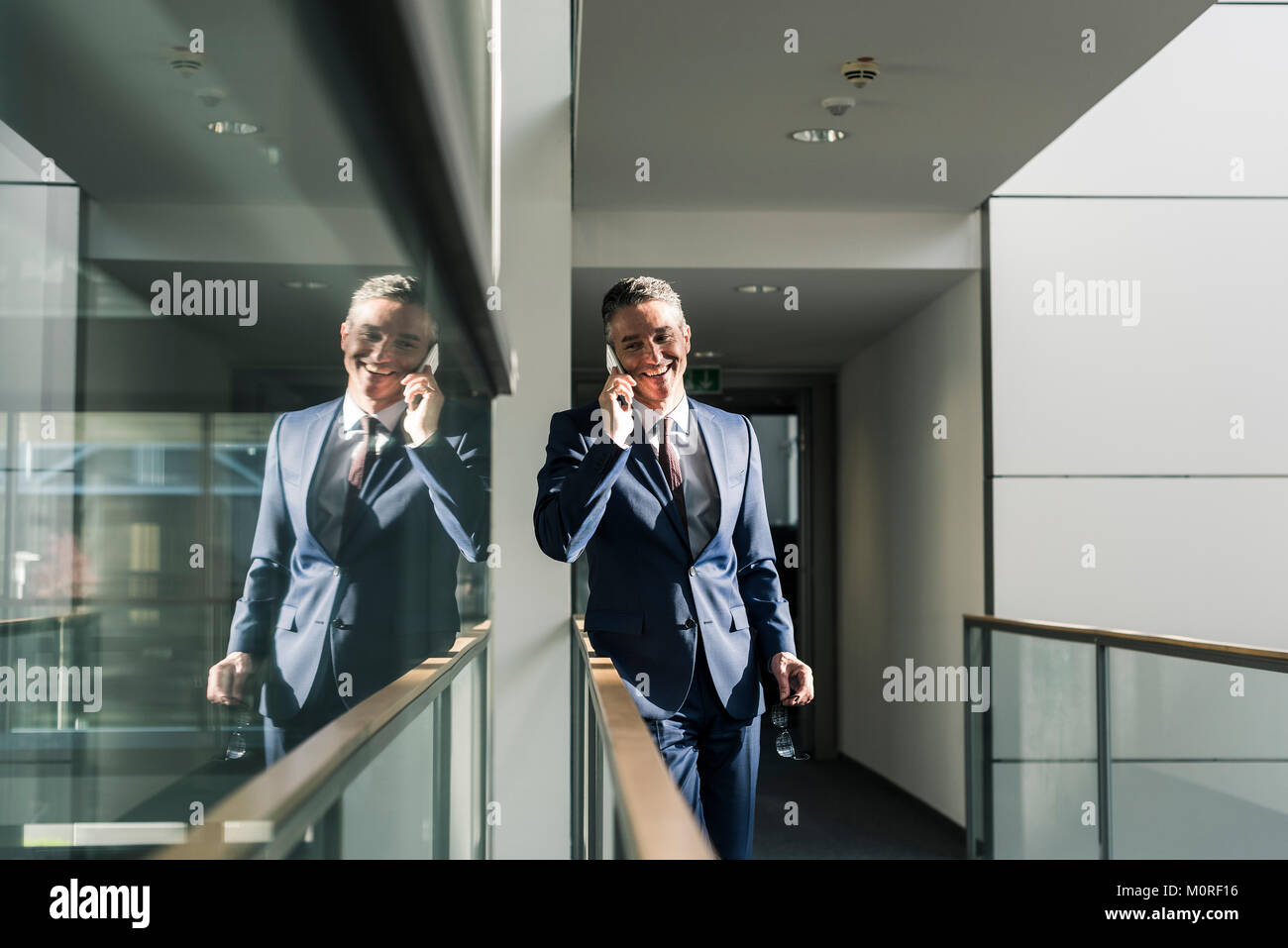 Imprenditore sorridente parlando al cellulare sul pavimento per ufficio Foto Stock