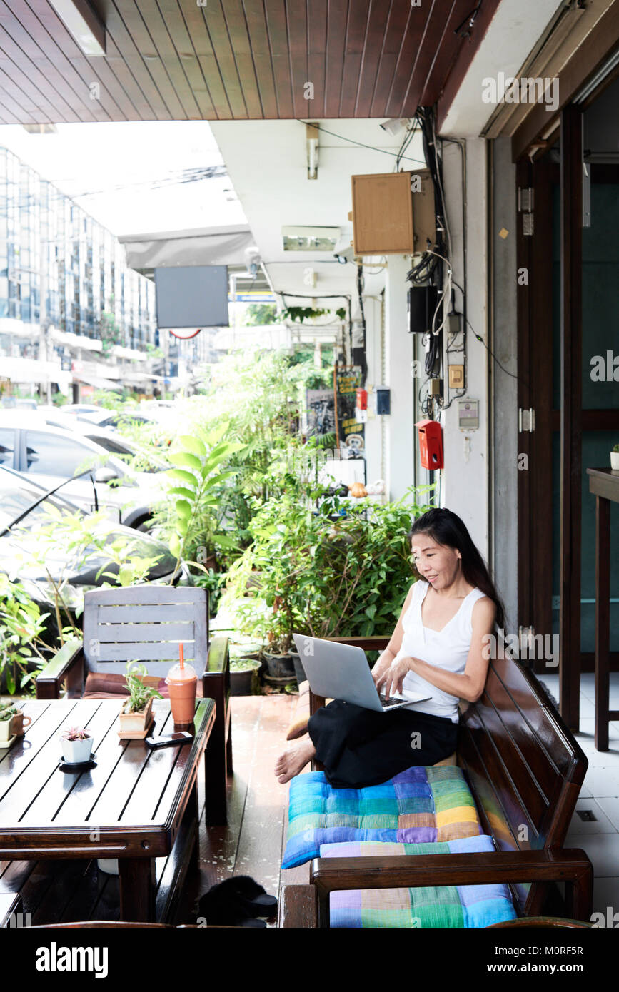 Bruna senior business donna lavora con il suo computer portatile al di fuori dell'ufficio sitted in un banco di colorati. Foto Stock