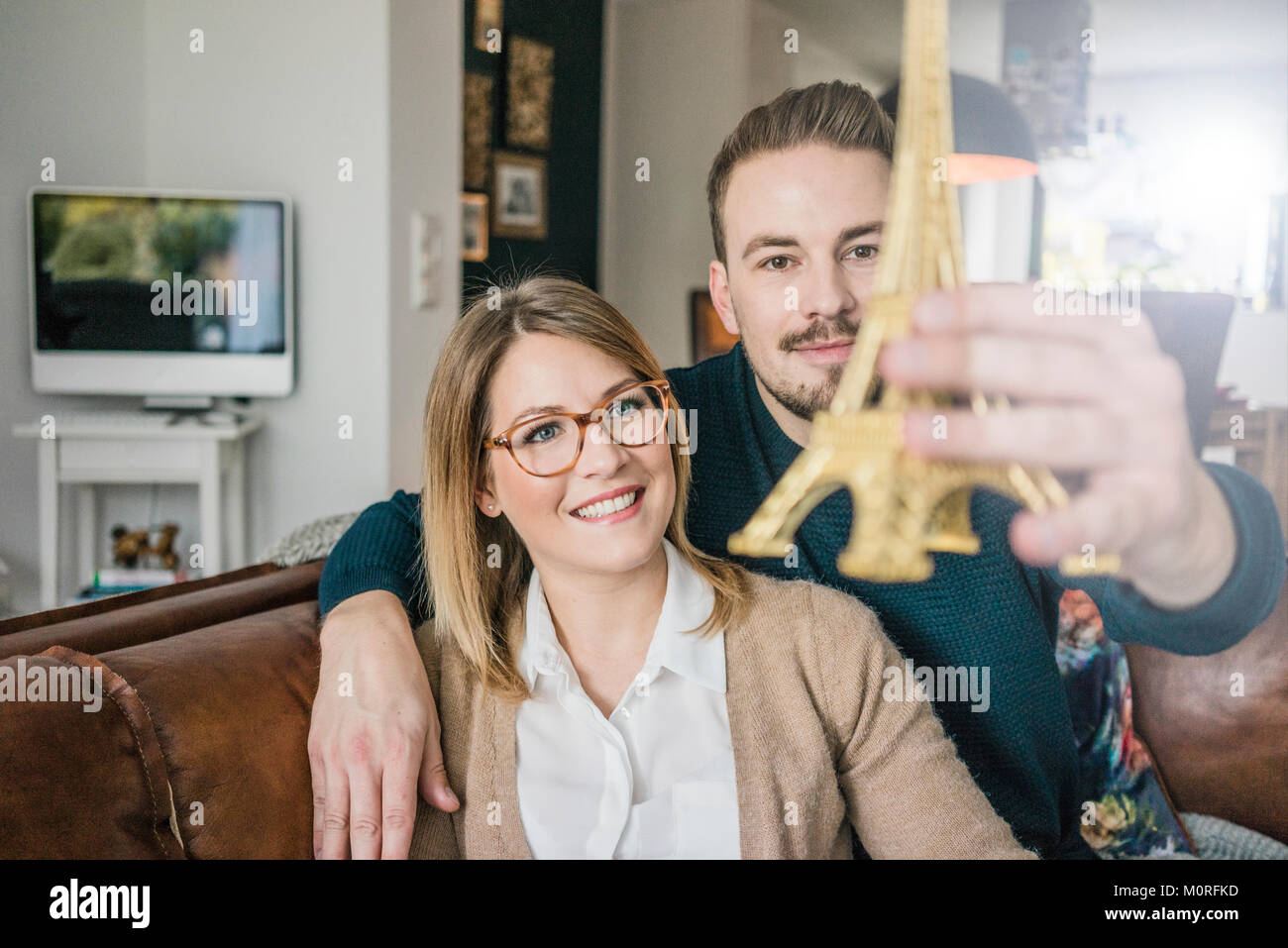 Sorridente giovane seduto sul divano di casa azienda Torre Eiffel modello Foto Stock